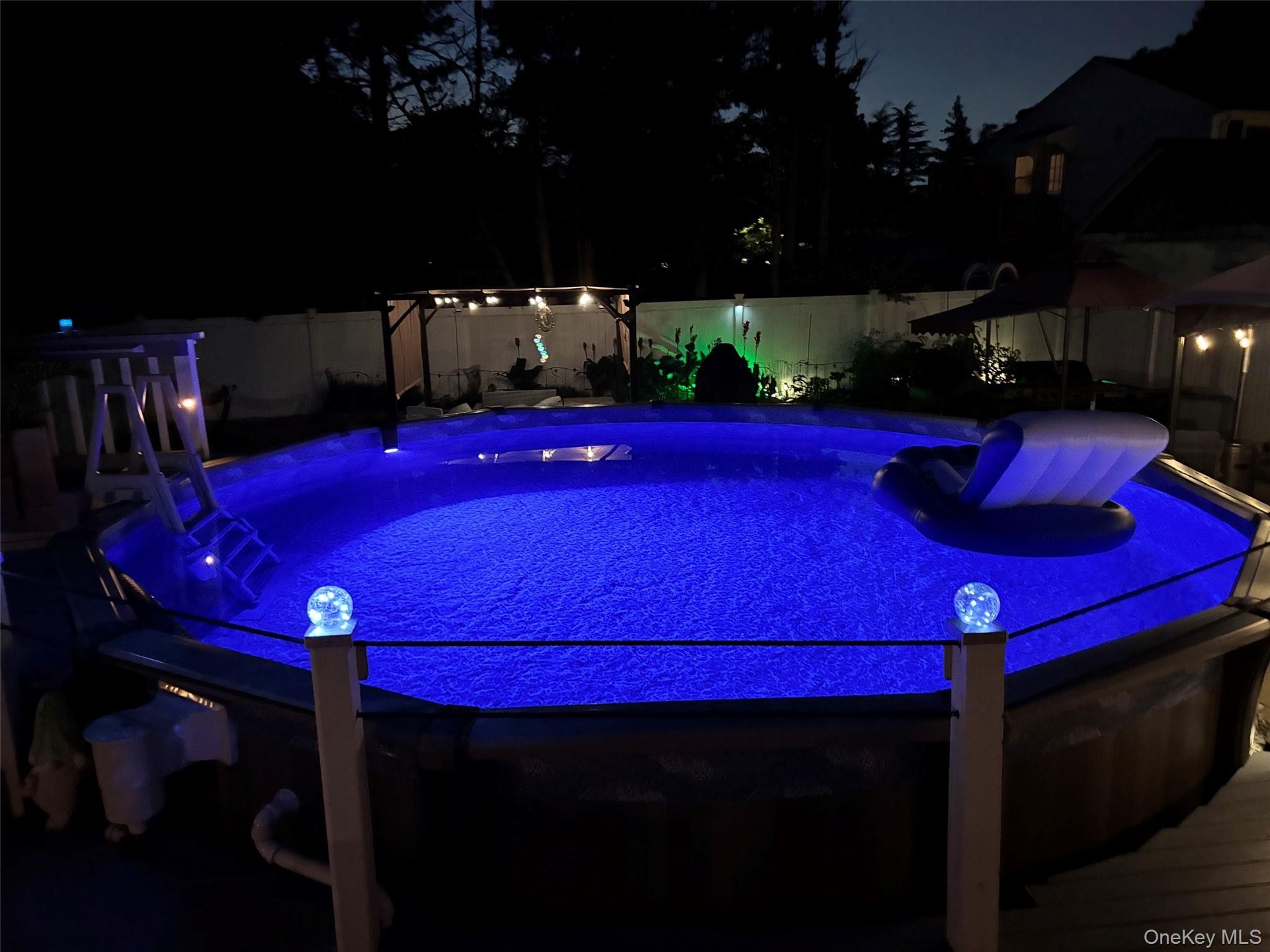 Outdoor pool featuring bright blue water, perimeter lighting, a deck surround, and a nearby pergola