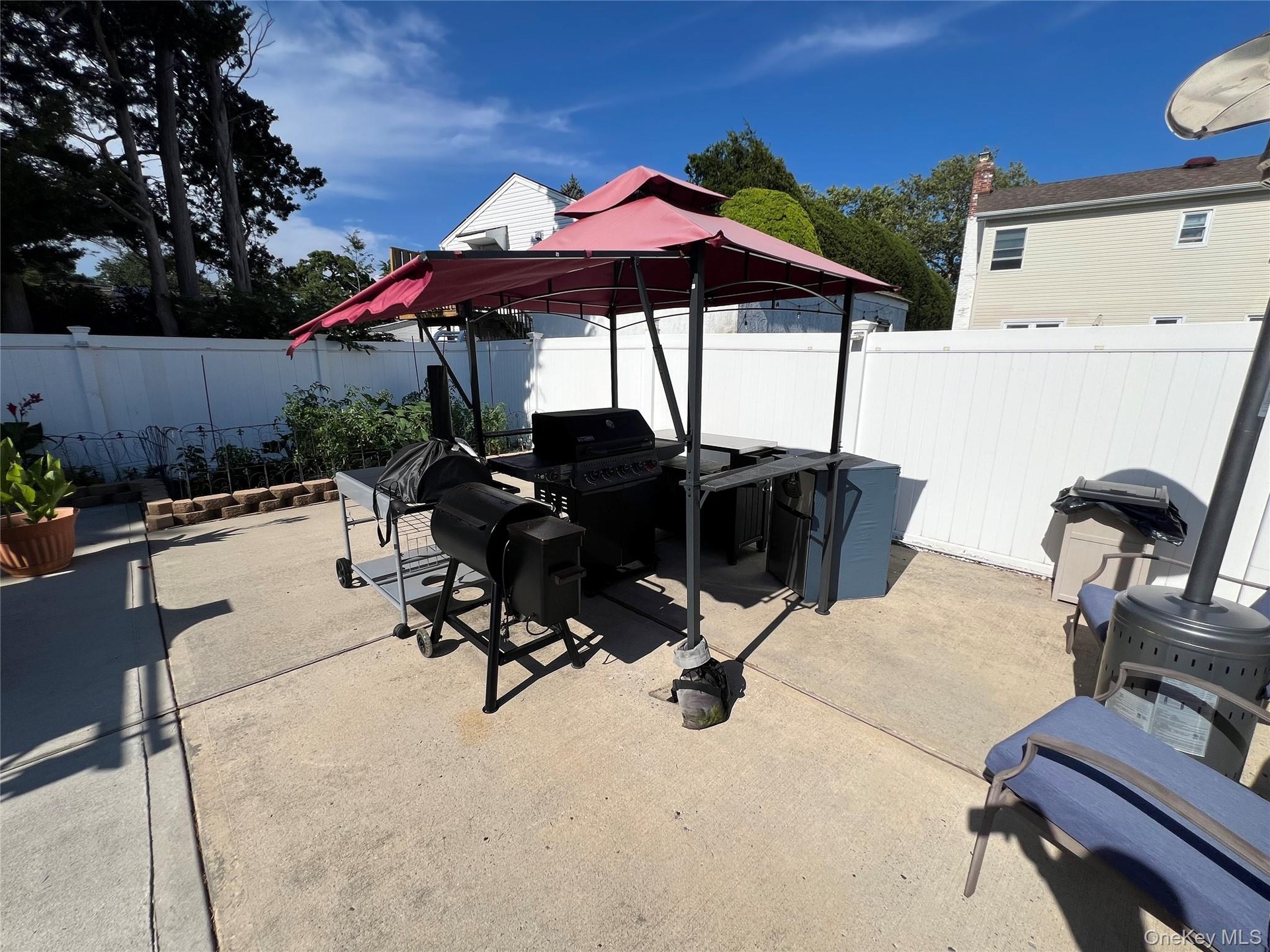 Paved patio area, white privacy fencing, and mature trees