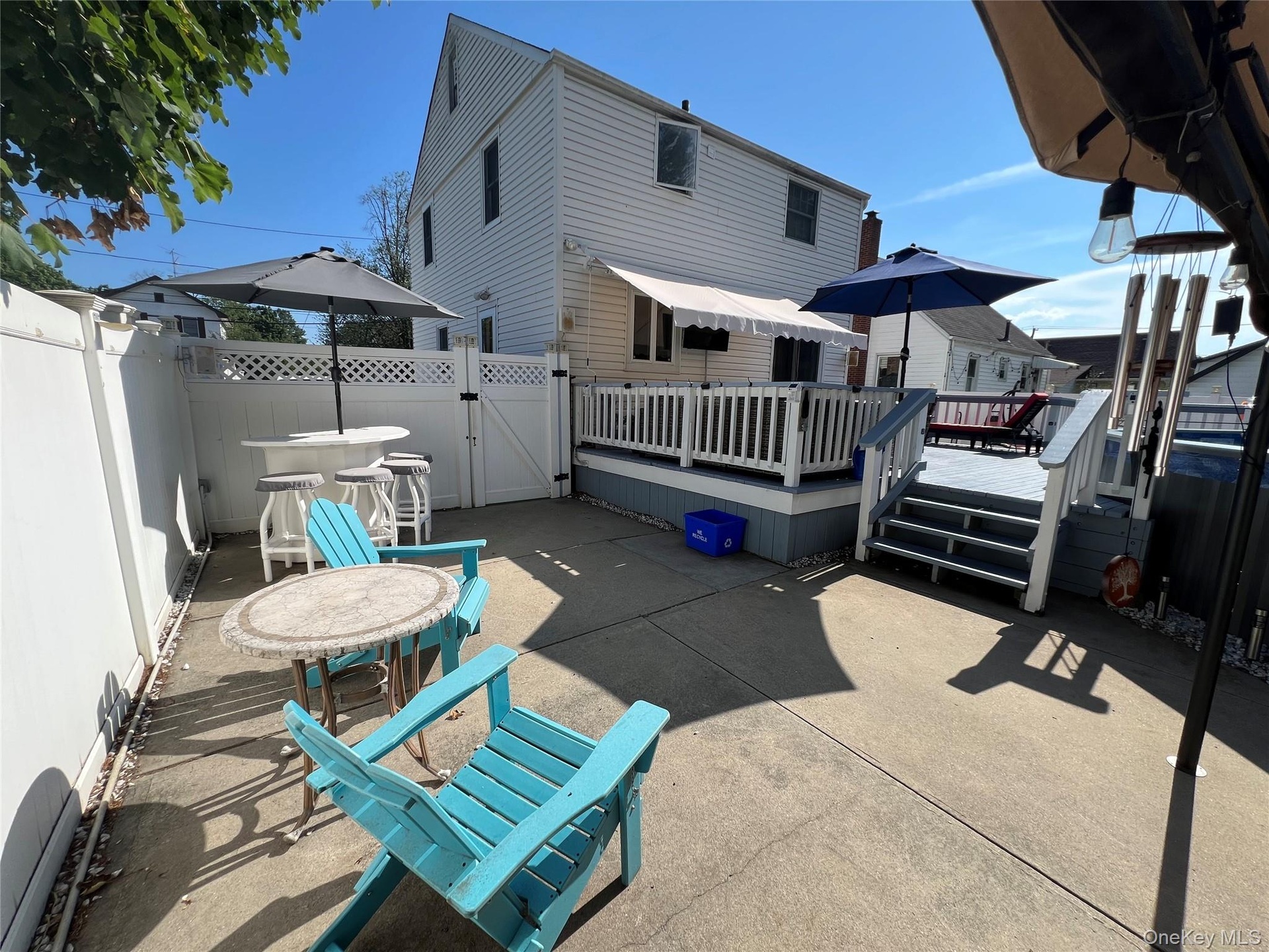 Private concrete patio with a raised wooden deck, white privacy fencing, and exterior siding