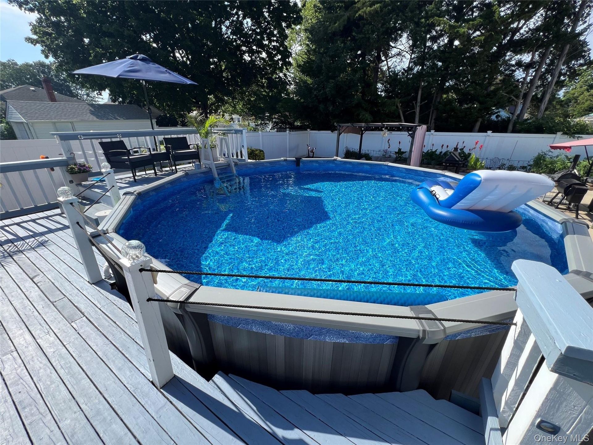 Expansive deck with an above-ground pool, featuring a white privacy fence and mature trees