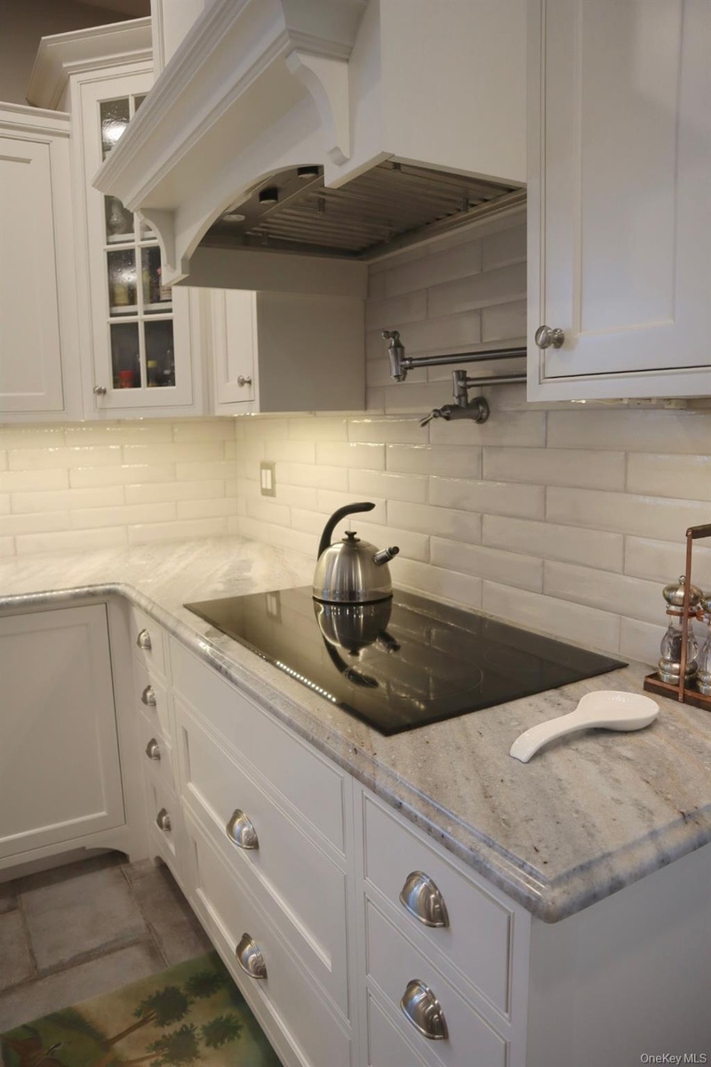 Kitchen featuring premium range hood, light stone counters, decorative backsplash, and white cabinets