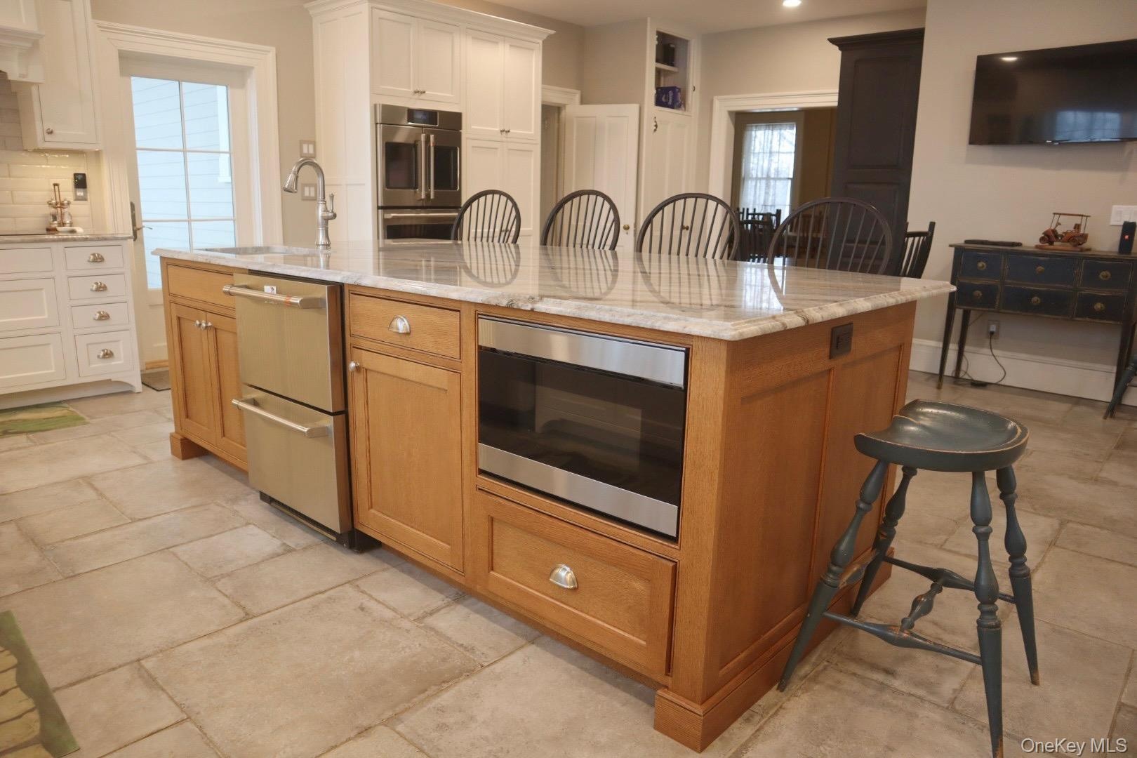 Kitchen featuring sink, white cabinetry, double oven, a large island, and light stone countertops
