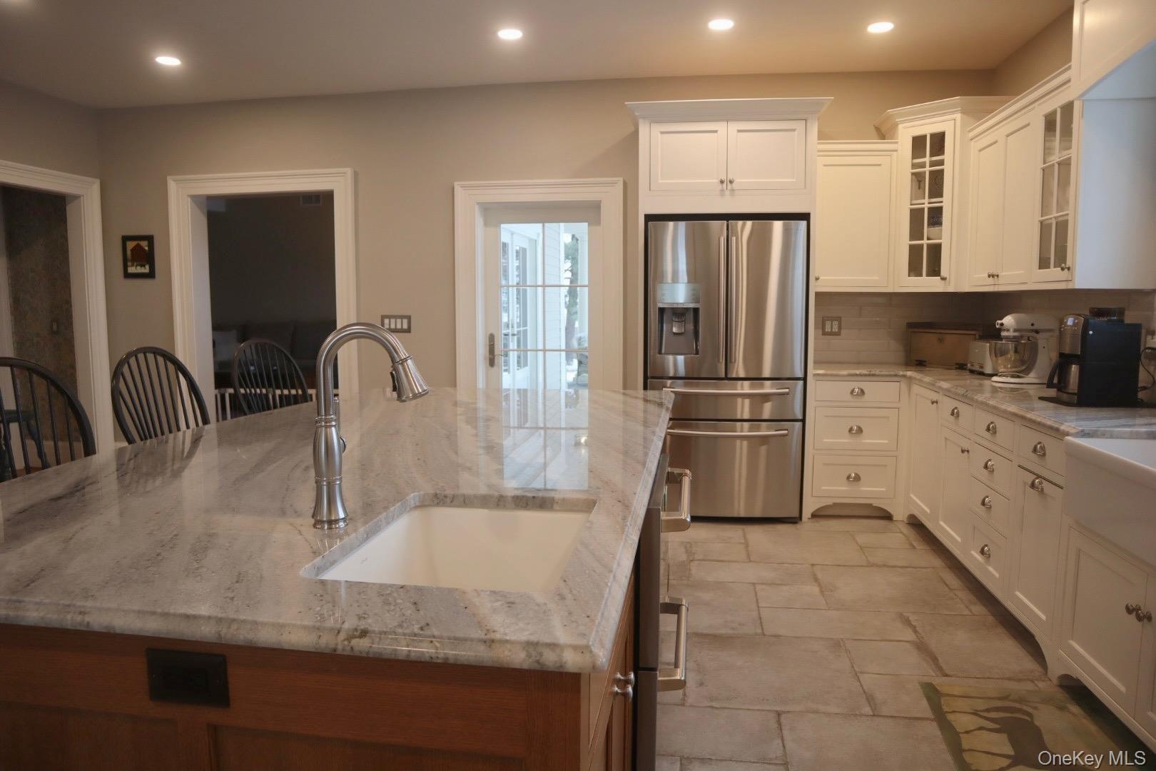 Kitchen with stainless steel refrigerator with ice dispenser, a kitchen bar, sink, and light stone counters