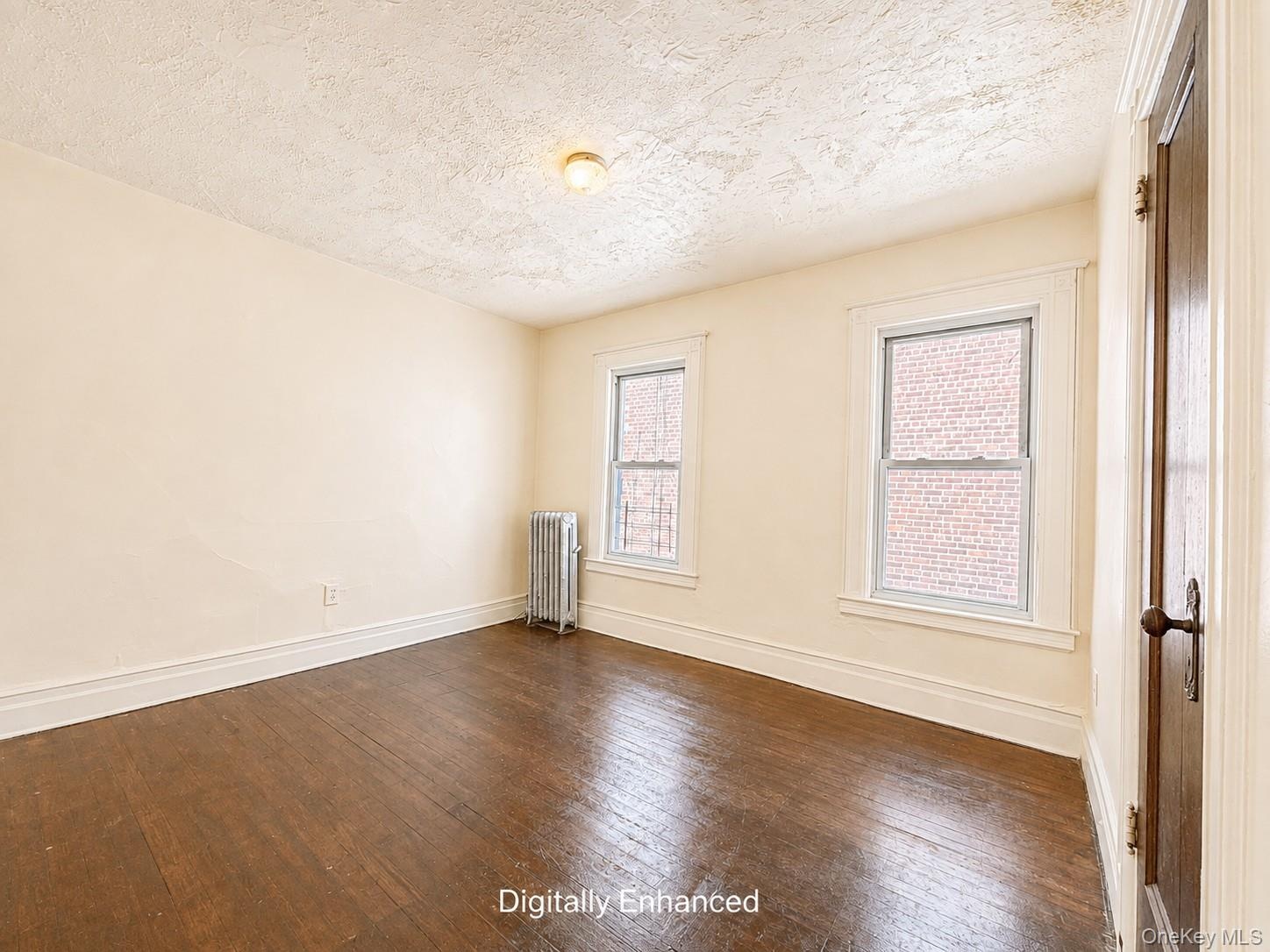 2nd fl  Hardwood flooring, two windows with white trim, wall-mounted radiator, and a wood panel door with dark hardware