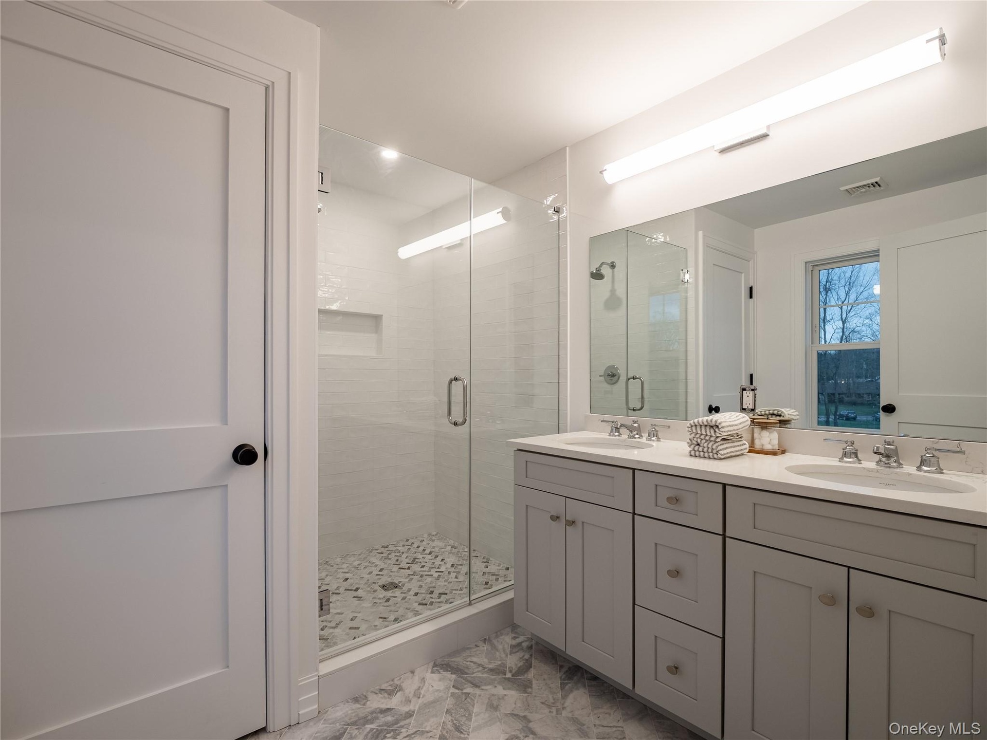 Bathroom featuring double vanity, a stall shower, and light marble finish flooring