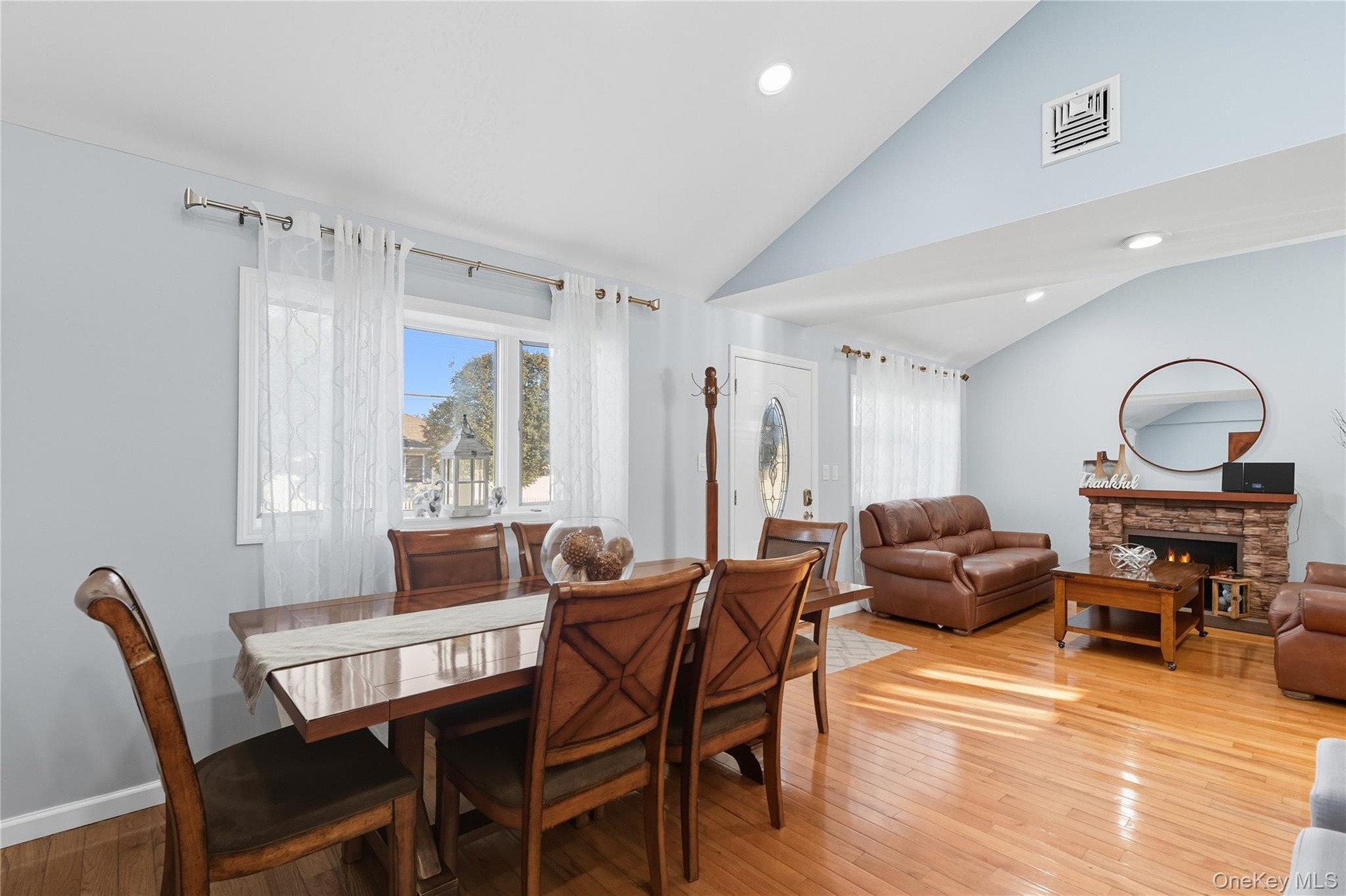 Dining area featuring light wood-type flooring, healthy amount of natural light, a stone fireplace, recessed lighting, and high vaulted ceiling