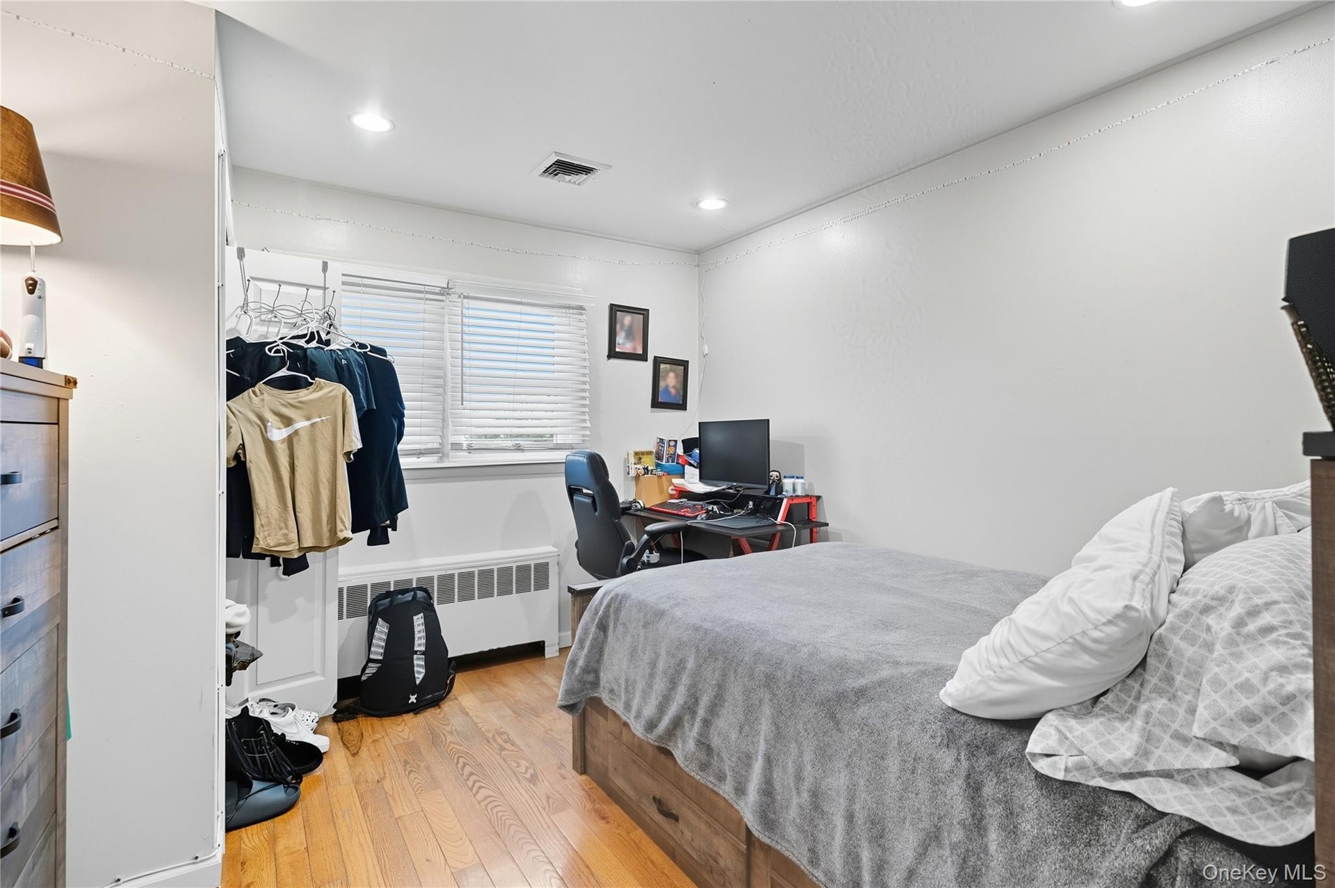 Bedroom with light wood-style floors, radiator heating unit, an office area, and recessed lighting