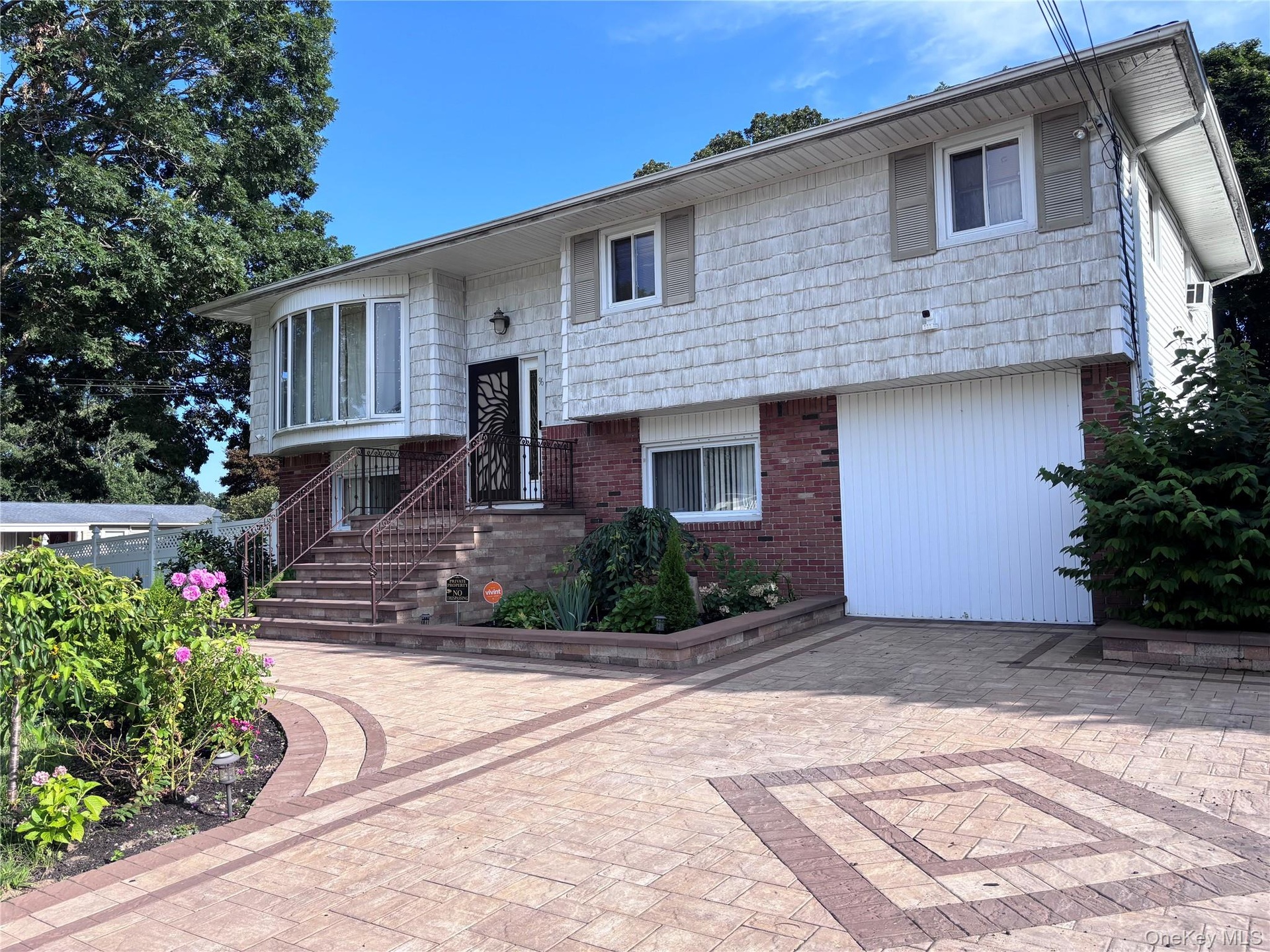 Split-level residence featuring a brick and shingle facade, bay window, and a patterned paver driveway