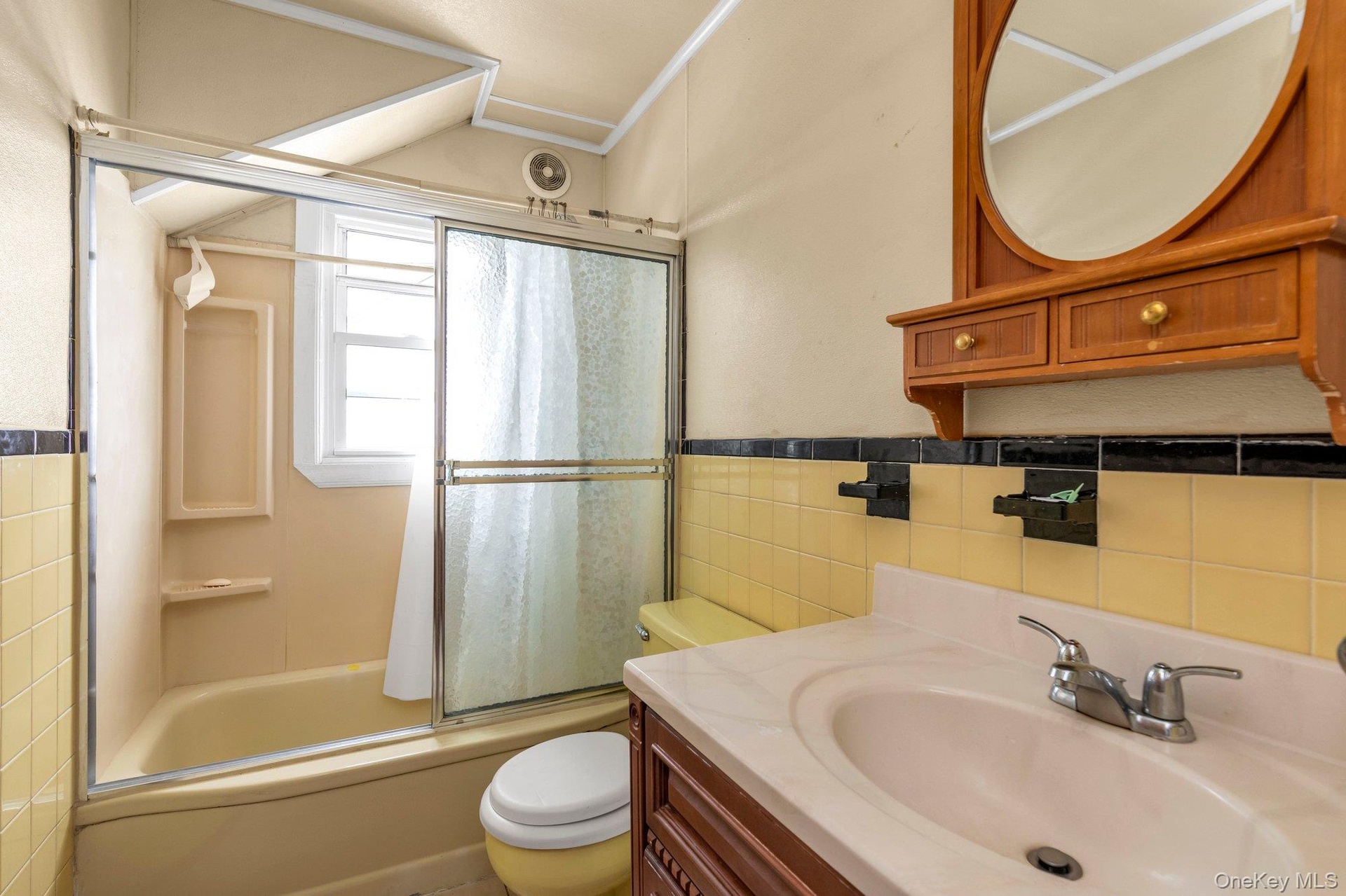 Bathroom featuring a built-in tub with a sliding glass enclosure, a vanity with an integrated sink, and a wall-mounted wooden medicine cabinet with an