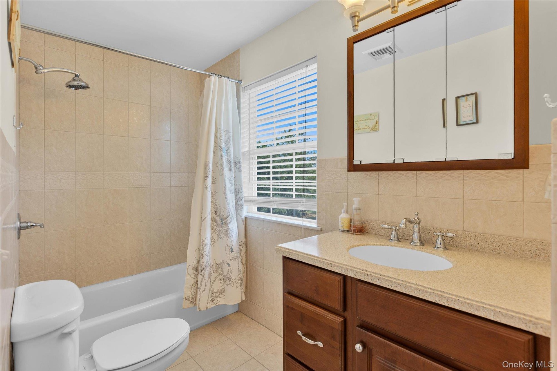 Bathroom featuring a built-in vanity and integrated sink, a tiled shower/tub combination, a window with blinds, and a mirrored medicine cabinet