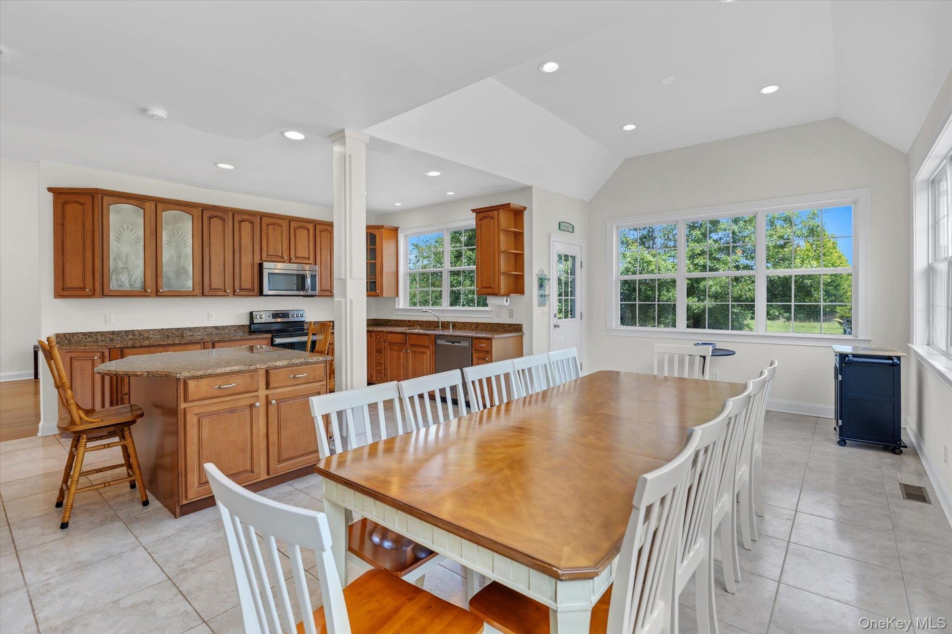 Expansive kitchen and dining area featuring wood cabinetry, stainless steel appliances, a kitchen island with seating, and tile flooring