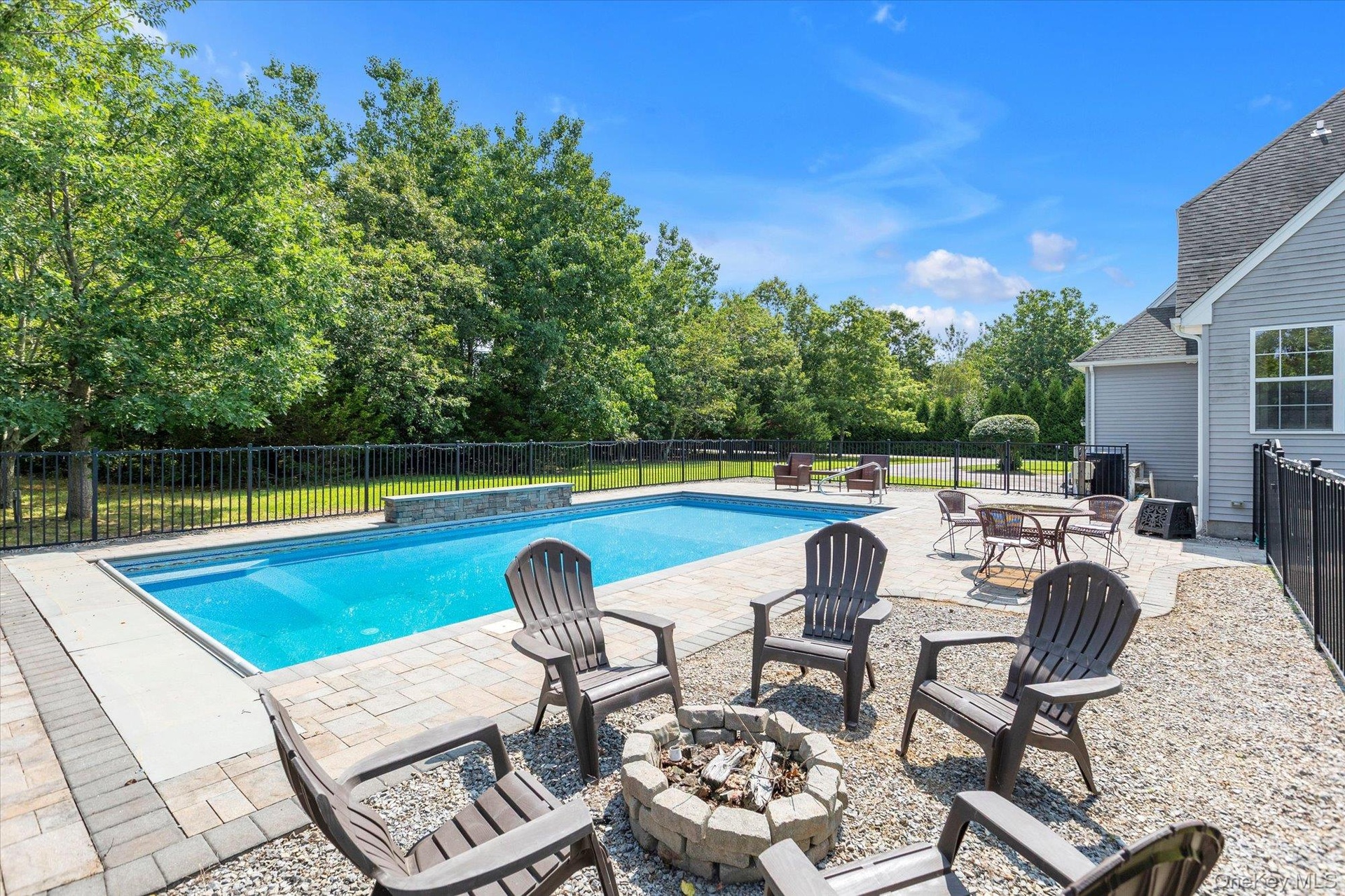 In-ground swimming pool with stone coping, paver patio, stone fire pit, and black fencing