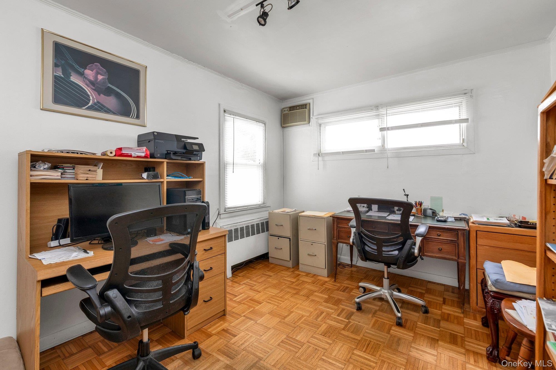 Parquet wood-finish flooring, two window openings, track lighting fixture, and white wall finishes bedroom or office