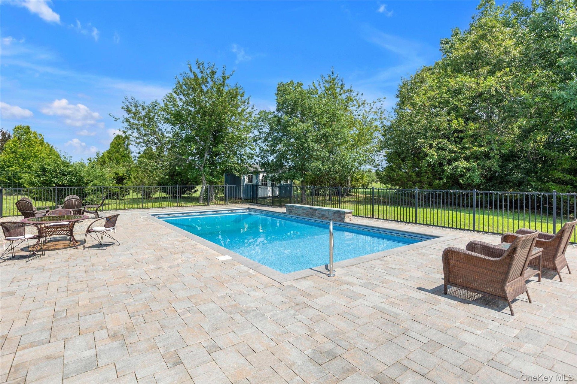 Outdoor pool area featuring a rectangular pool, paver patio, black metal fencing,