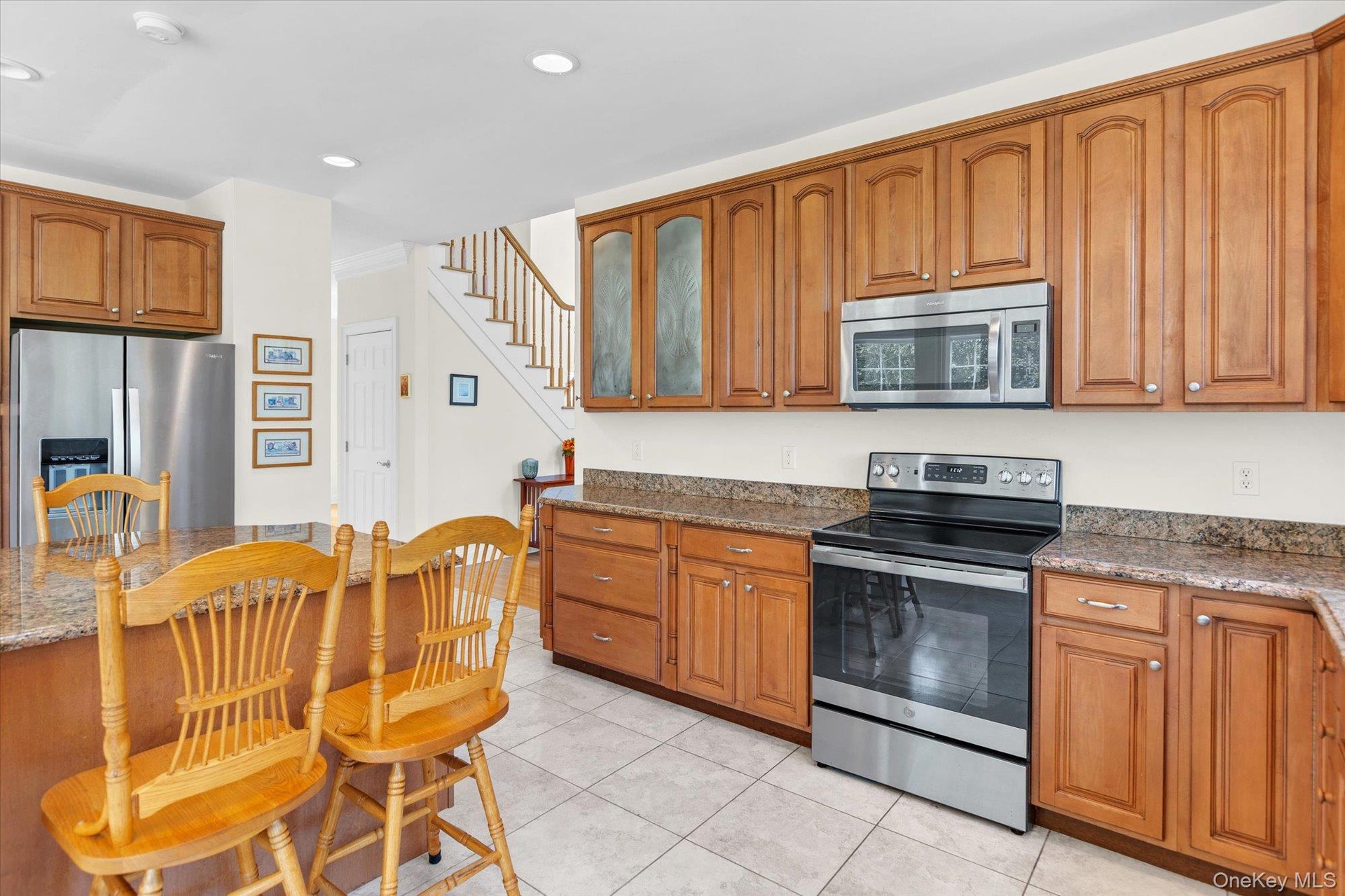 Kitchen featuring stainless steel appliances, wood cabinetry, granite-style countertops, and tile flooring