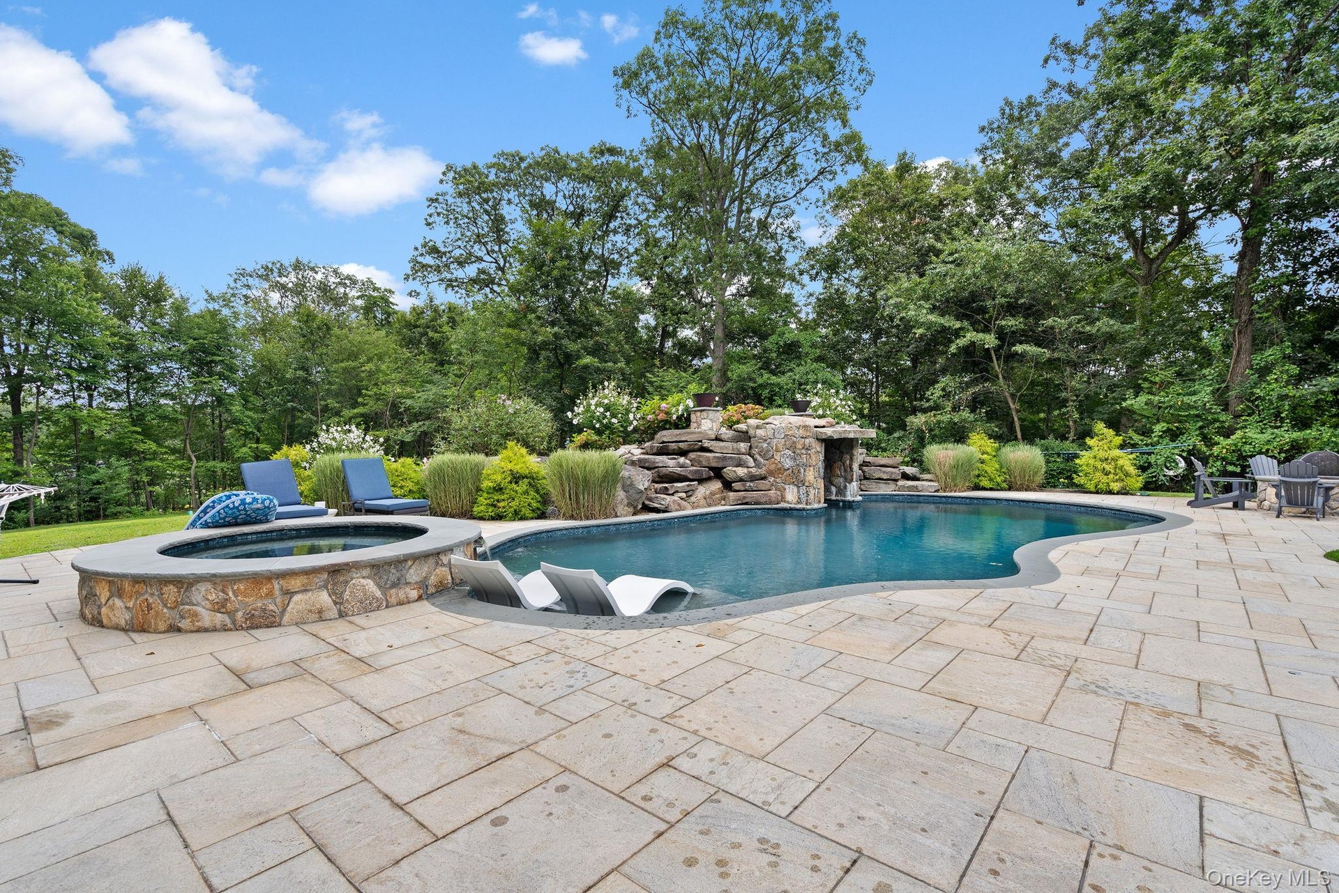 Outdoor pool featuring a patio area, an in-ground hot tub, and view of wooded area