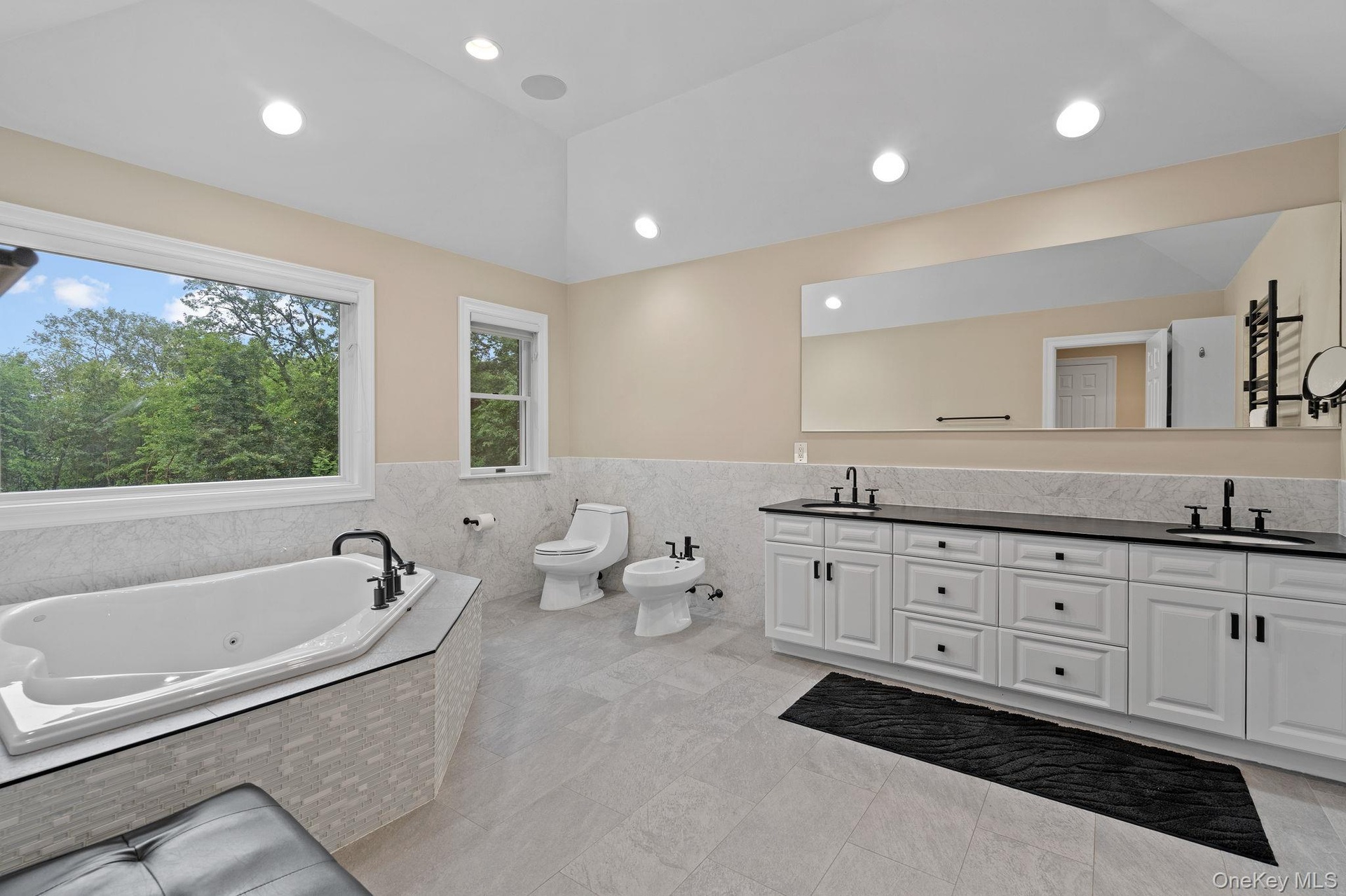 Full bathroom featuring tile walls, a jetted tub, double vanity, wainscoting, and a bidet
