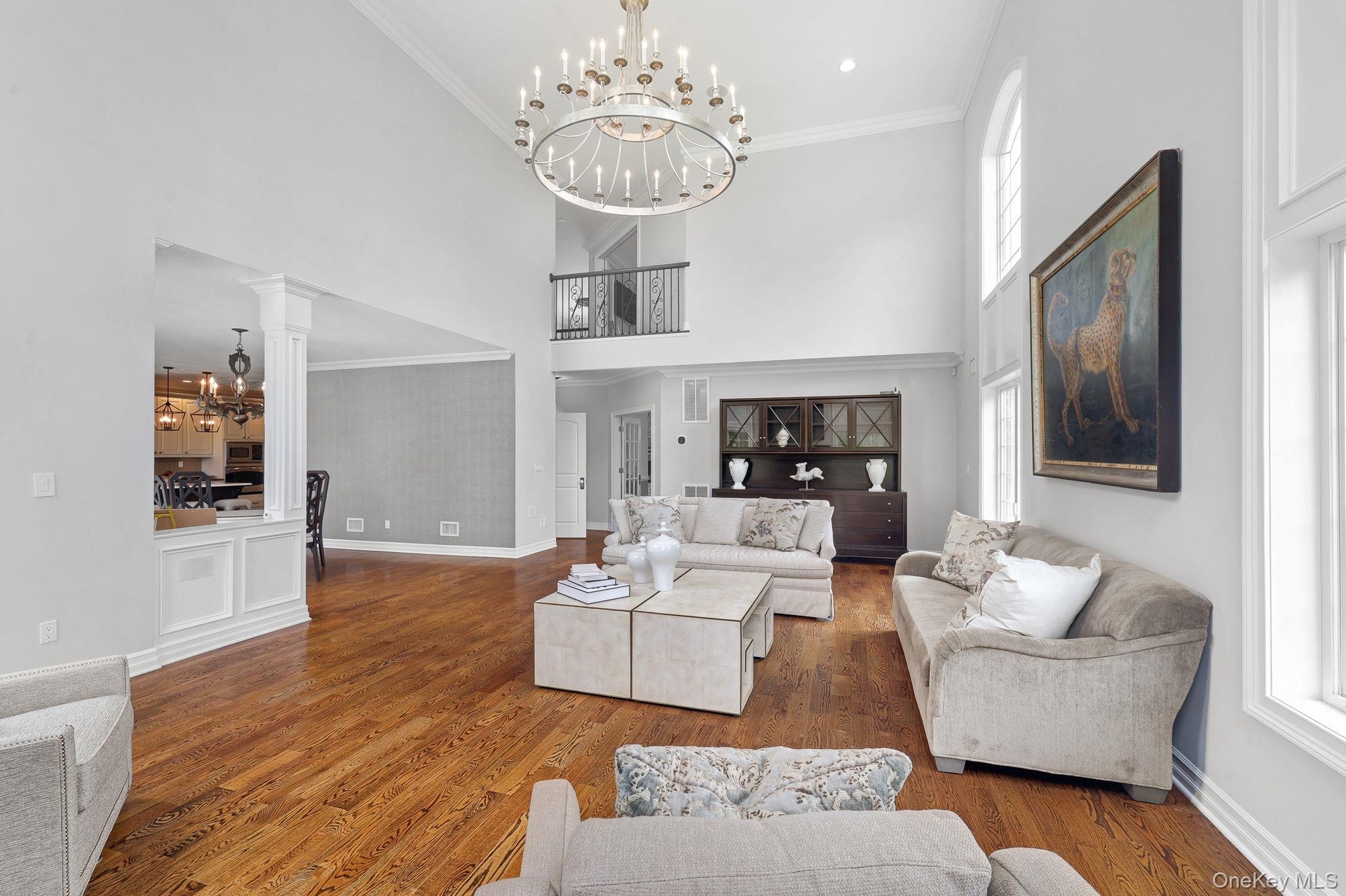 Two-story living area featuring hardwood flooring, a multi-tiered chandelier, tall arched windows, and a second-story balcony