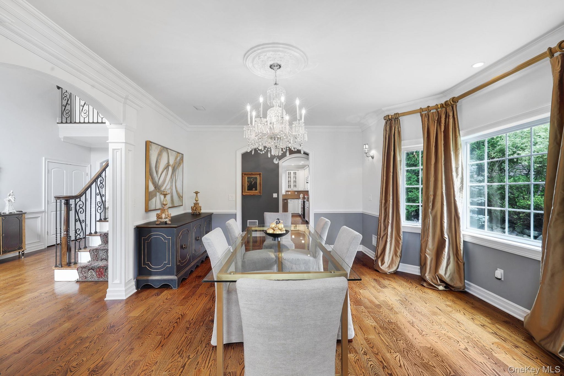 Hardwood flooring, chandelier with ceiling medallion, decorative wall sconces, columned archway, and wrought iron stair railing