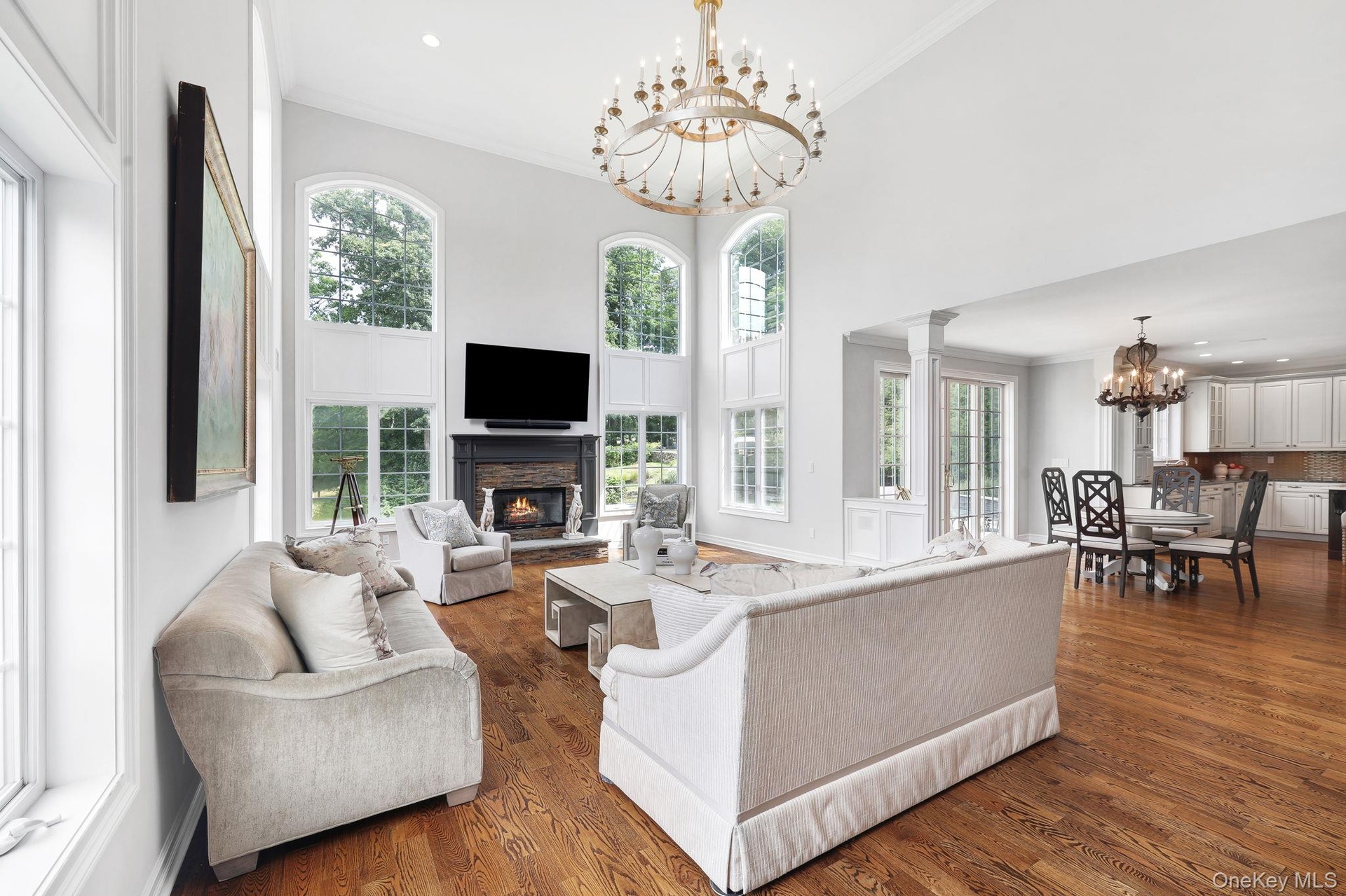 Two-story living area with hardwood flooring, a fireplace featuring a dark mantel, and multiple arched windows