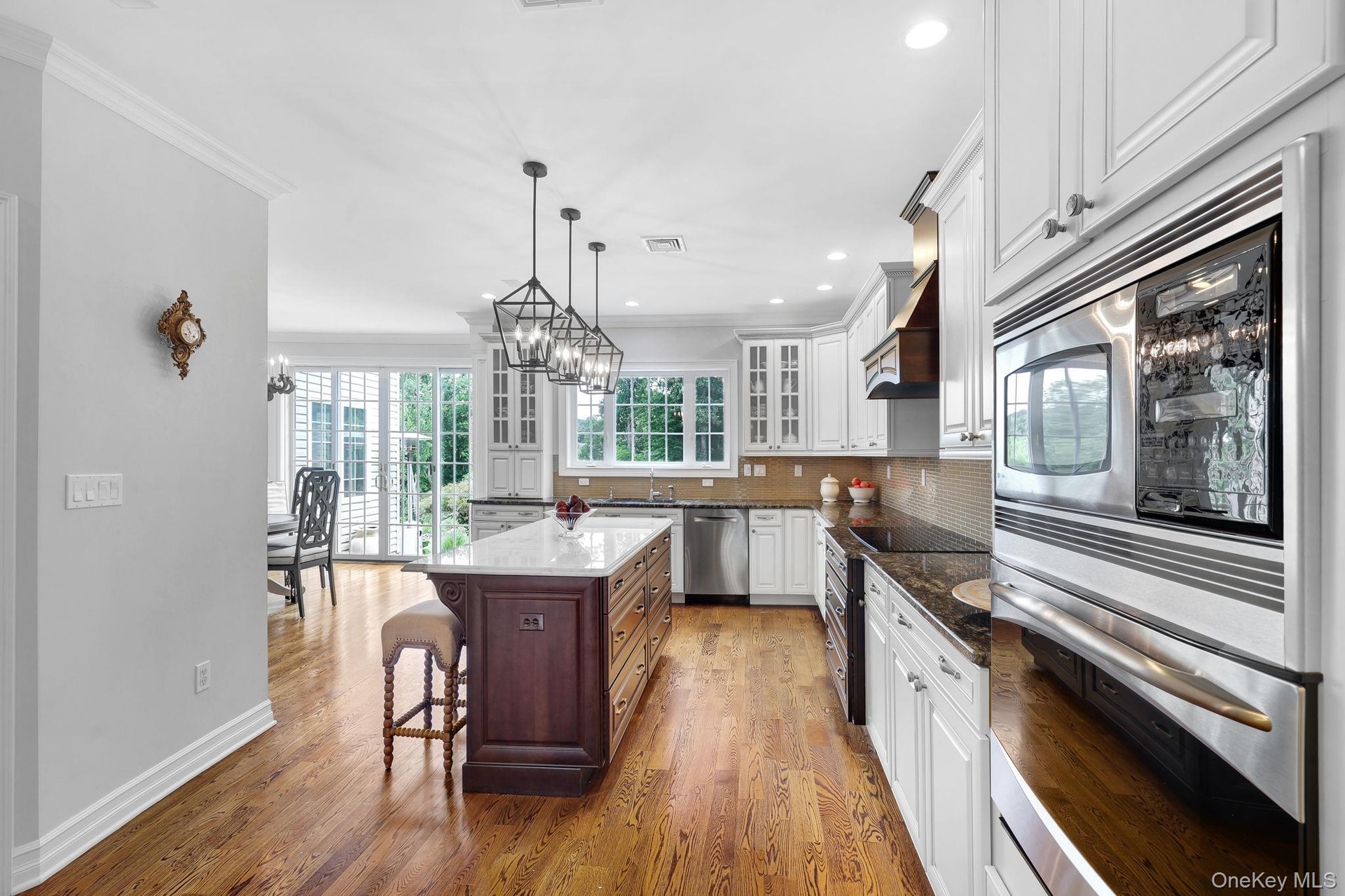 Kitchen featuring wood-finish flooring, white cabinetry, a dark wood-finish island with a light-toned countertop, and stainless steel built-in applian