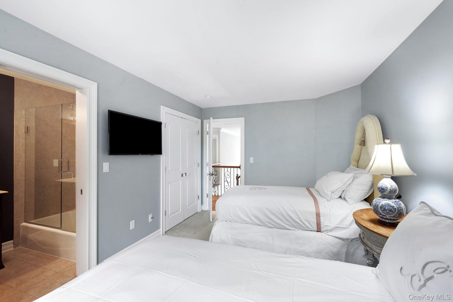 Light-toned wall paint, light wood-finish flooring, white paneled doors, and an en-suite bathroom with a glass-enclosed shower over tub