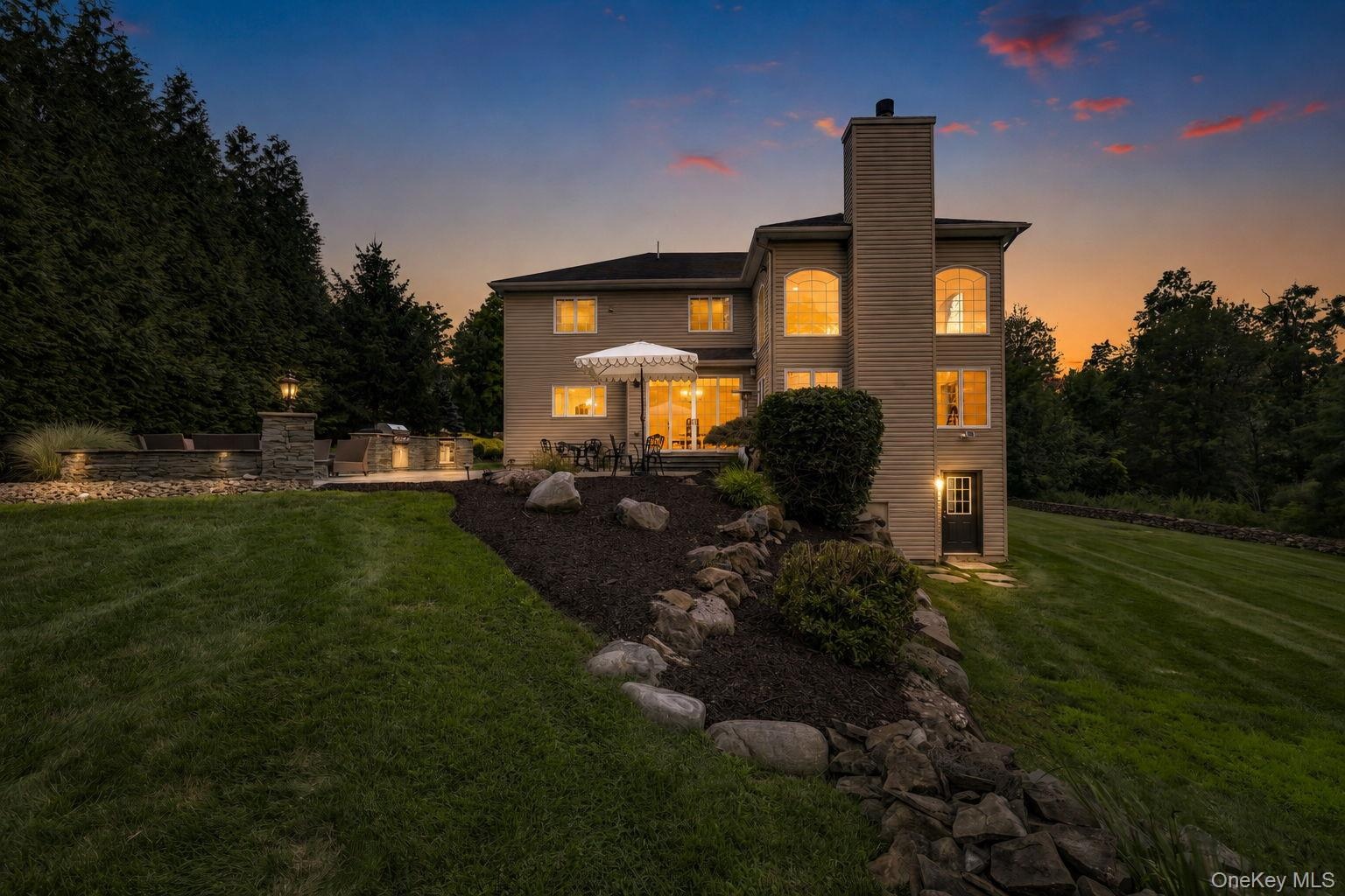 Extensive backyard with a manicured lawn, a stone retaining wall, and a multi-level patio featuring a built-in kitchen/grill station