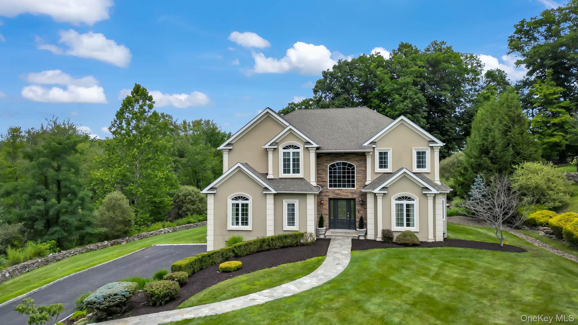 Stately two-story Colonial with cream exterior and dark roof, featuring a symmetrical facade with multiple arched and rectangular windows, a centered 