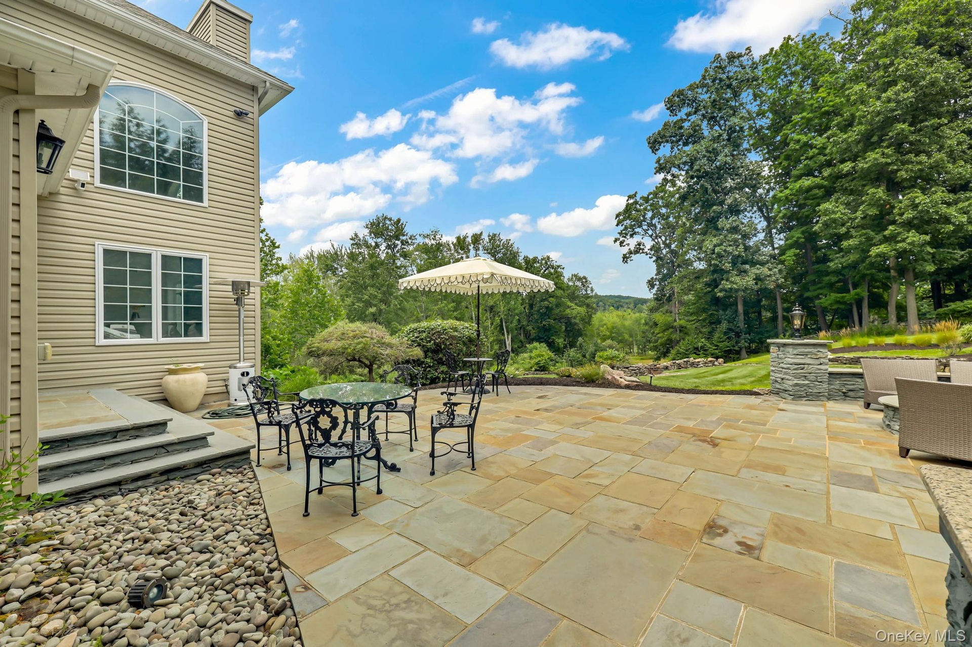 Expansive paver patio with stone retaining walls, stone steps, and a large arched window