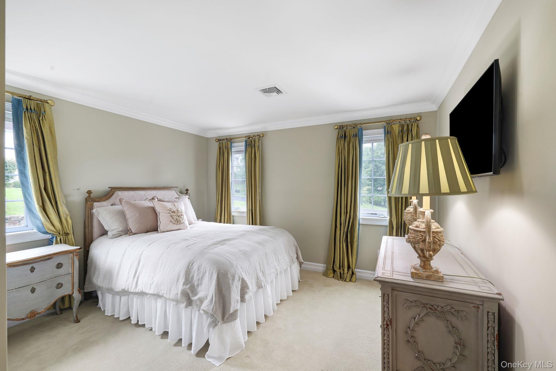 Elegant primary bedroom featuring multiple windows with natural light, neutral wall finishes, and wall-mounted flat-screen television