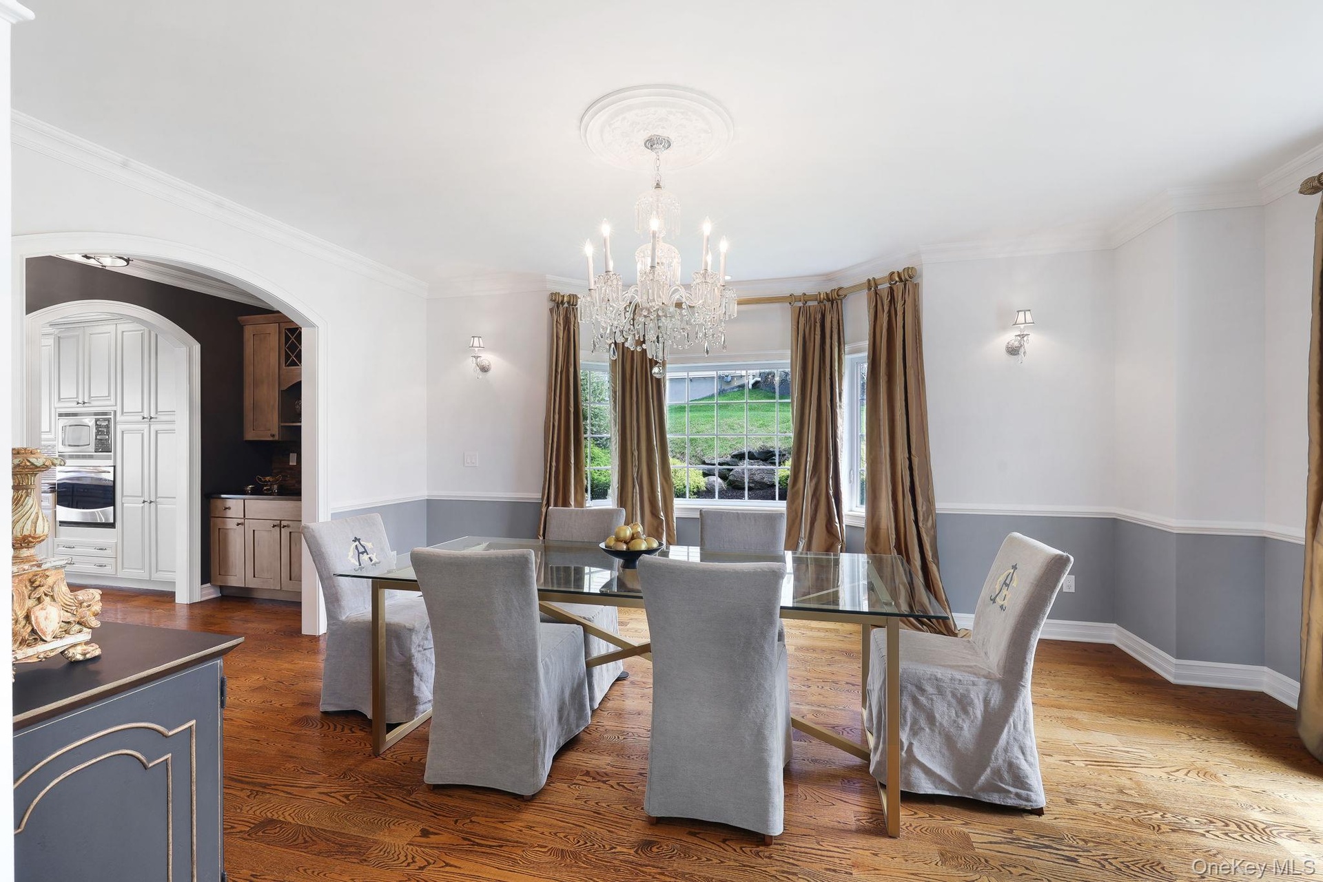 Hardwood flooring, arched doorway, built-in kitchen cabinetry, decorative ceiling medallion, and wall sconces