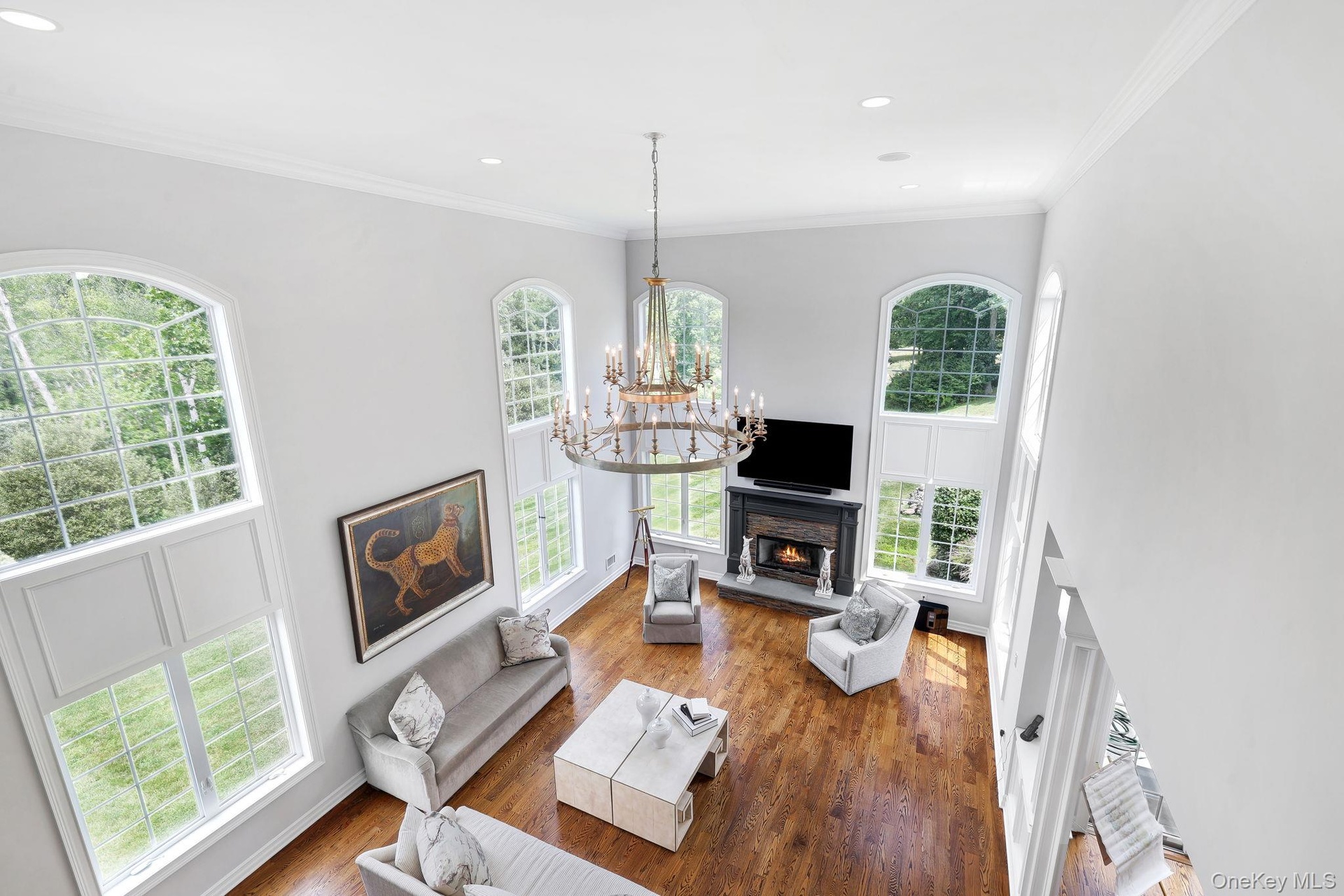Two-story living area featuring hardwood flooring, a central chandelier, and a fireplace with a stone surround