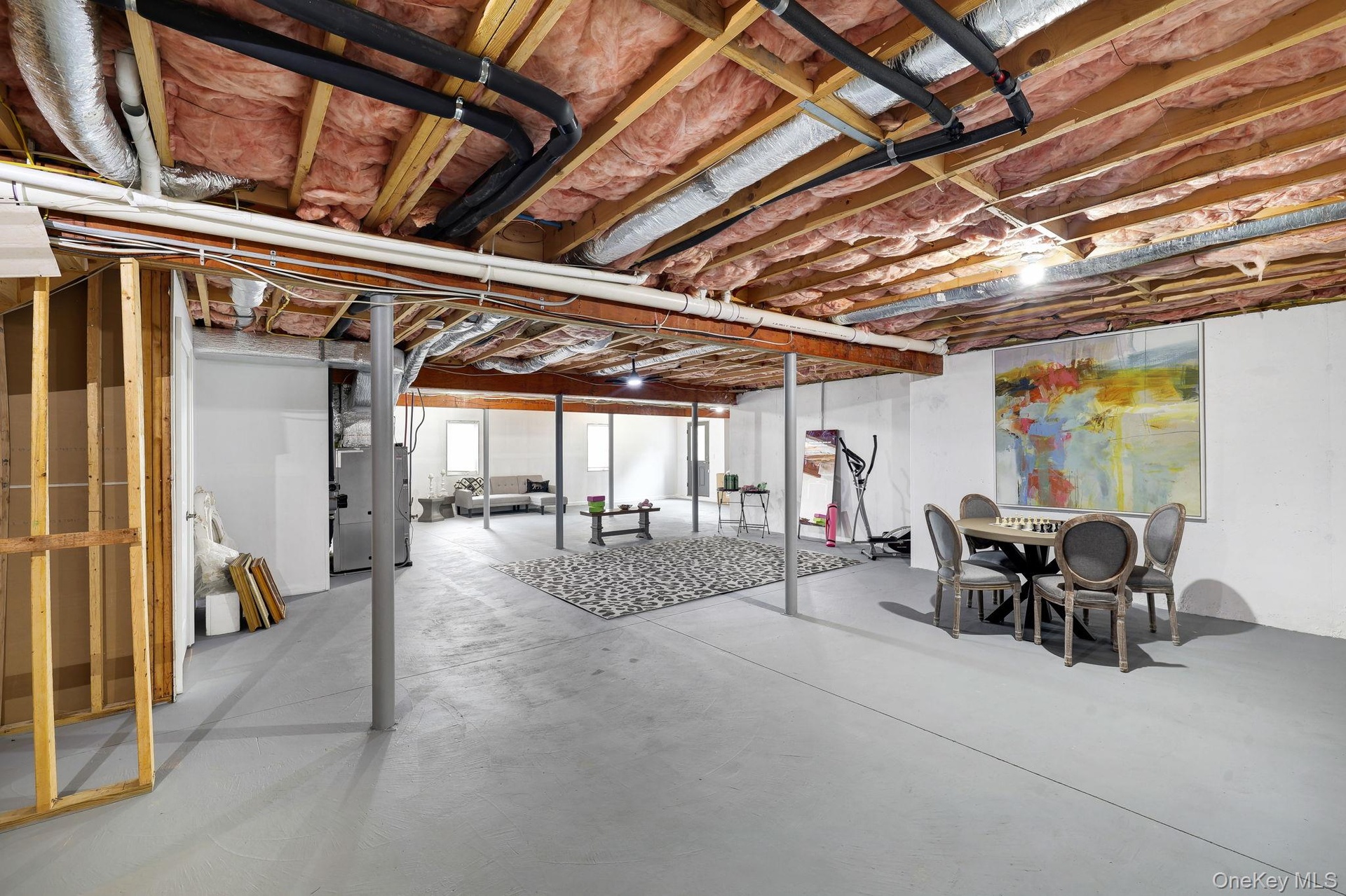 Spacious unfinished basement with exposed wooden joists, concrete flooring, and metal support columns