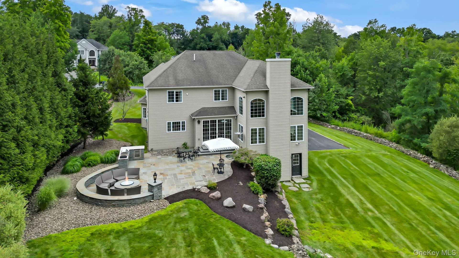 Expansive stone patio with built-in seating area and fire pit and extensive backyard.