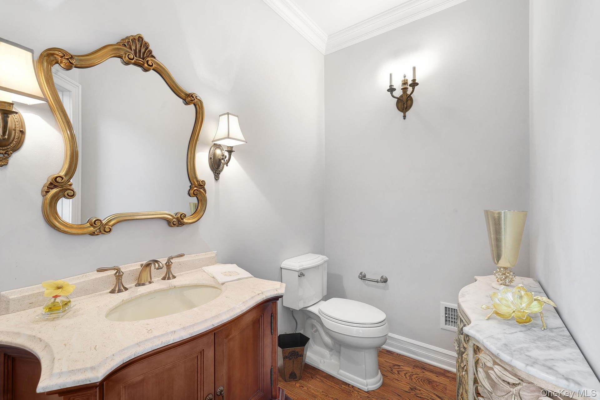 First floor bathroom featuring a wood vanity with a light-toned countertop, an ornate gold-framed mirror, and wood-finish flooring