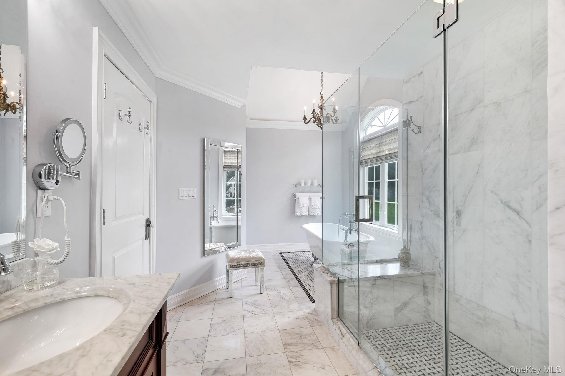 Marble-finish flooring, glass-enclosed shower with tile base, freestanding bathtub, and a double-hung arched window