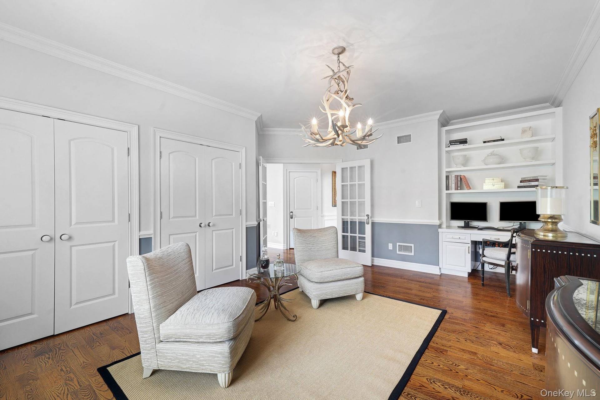 Hardwood flooring, custom built-in shelving, crown molding, double doors, and a decorative antler chandelier