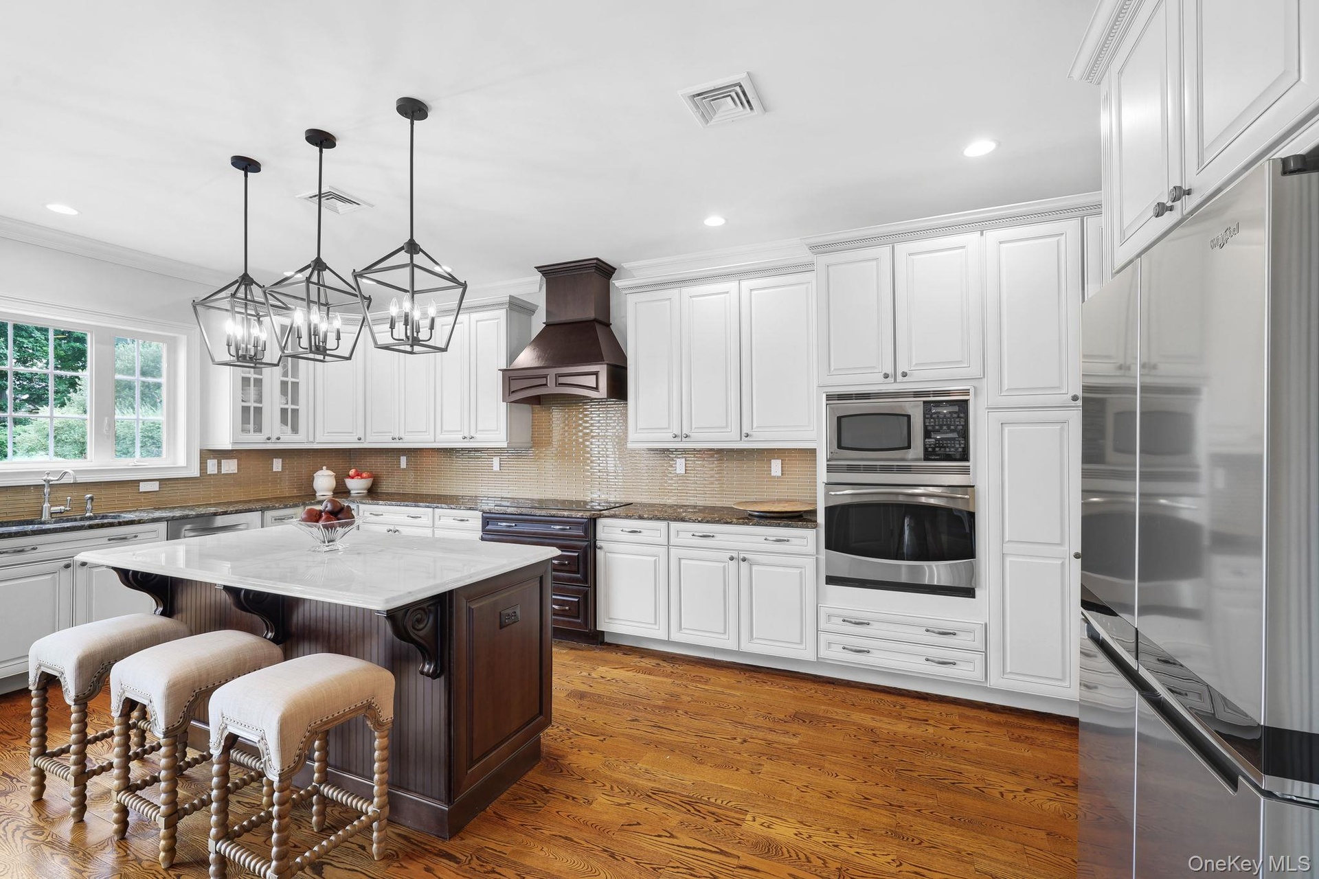 Kitchen featuring hardwood flooring, a central island with a light-toned countertop, white cabinetry, a built-in microwave and oven, and stainless ste