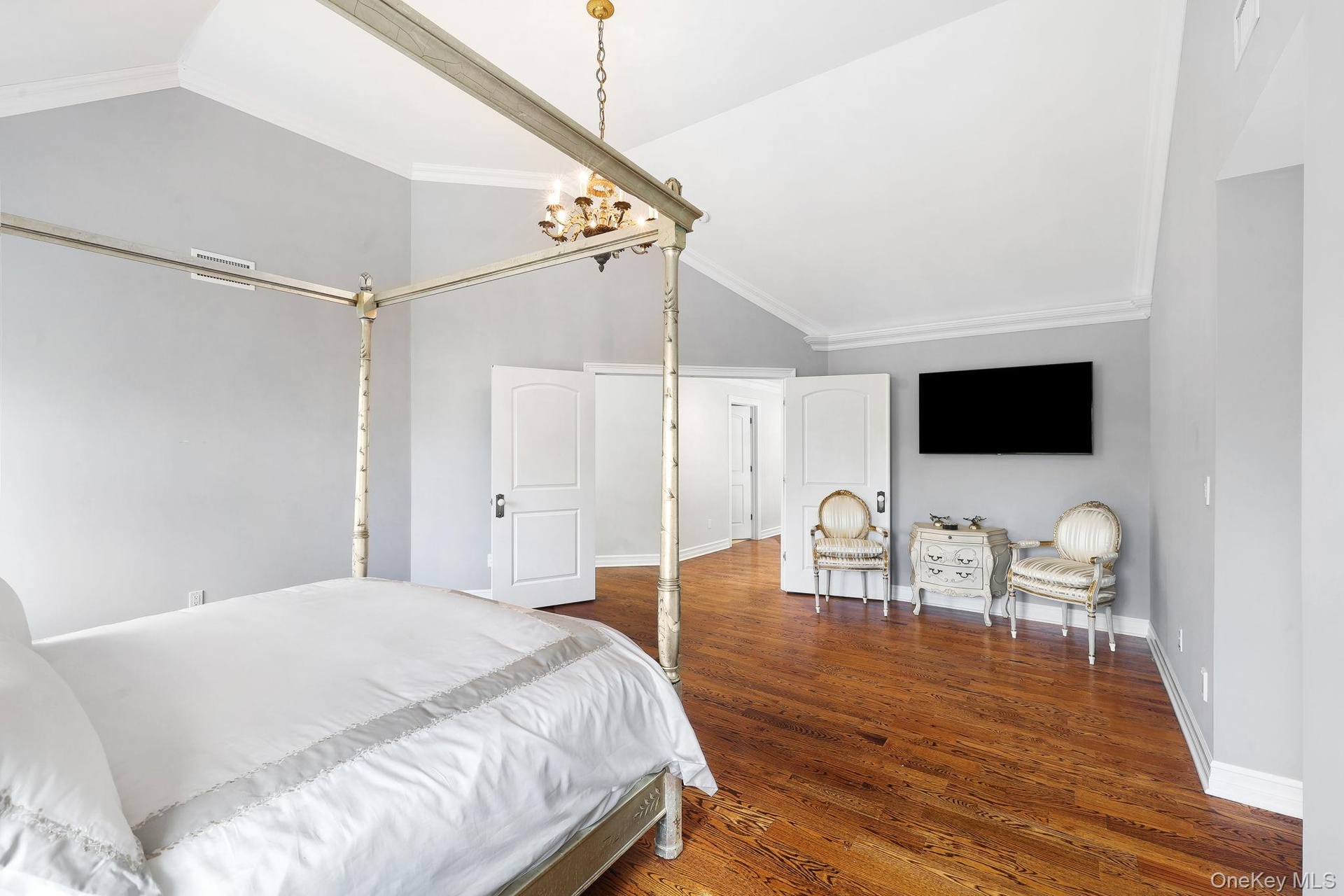 Hardwood flooring, vaulted ceiling, crown molding, white paneled doors, and a gold-tone chandelier