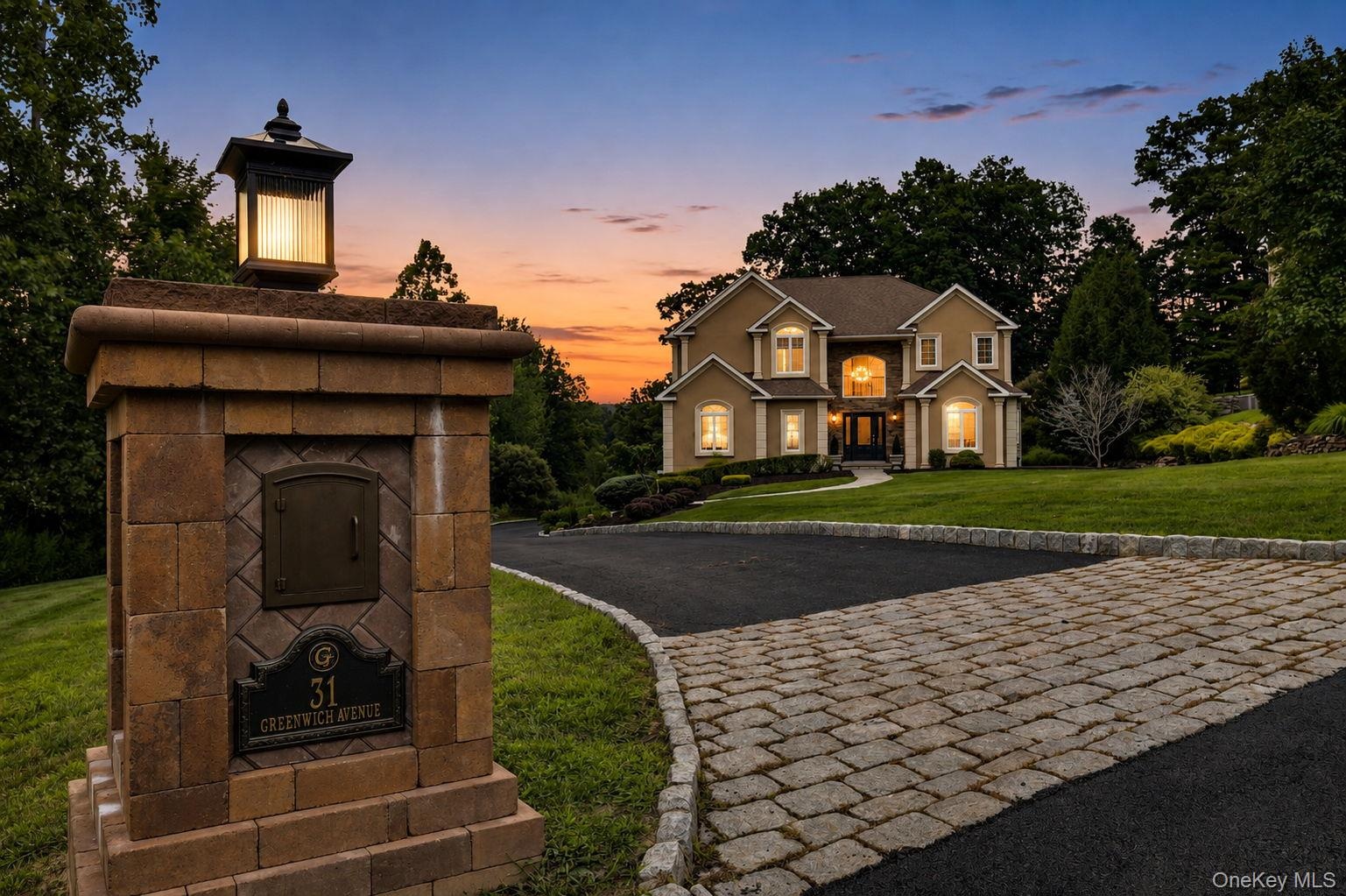 Belgium block curbing ,elegant custom stone and lighted mail box, custom pavers with evening view of  two-story residence exterior with multiple illum