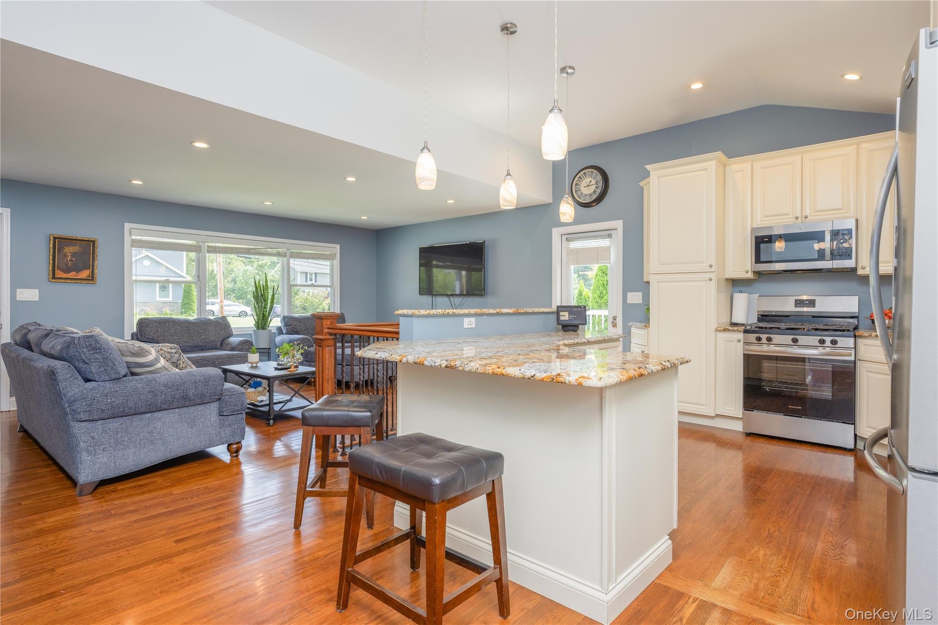 Open-concept living space featuring wood-finish flooring, recessed lighting, a kitchen island with stone countertop, and stainless steel appliances