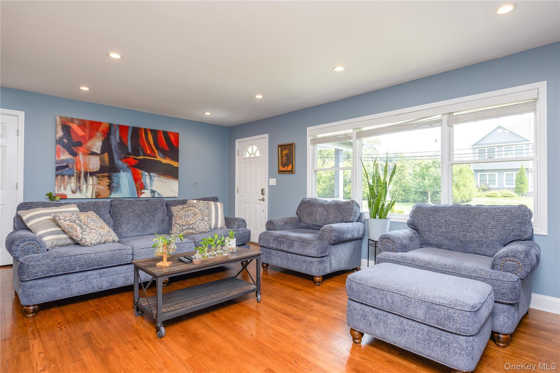 Recessed lighting illuminates the open living area featuring wood-finish flooring, a white paneled door, and a multi-pane window