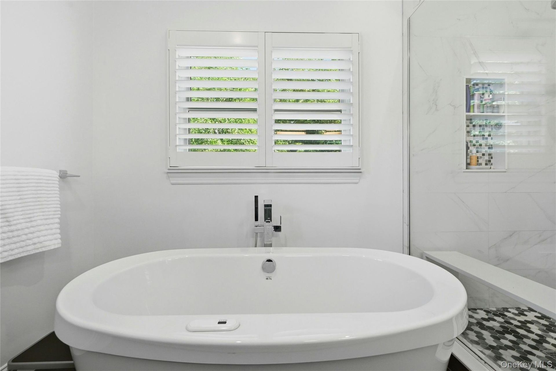 Spa-inspired primary bath featuring a freestanding oval soaking tub, marble-look wall tile surround, polished stone-look flooring with geometric mosai