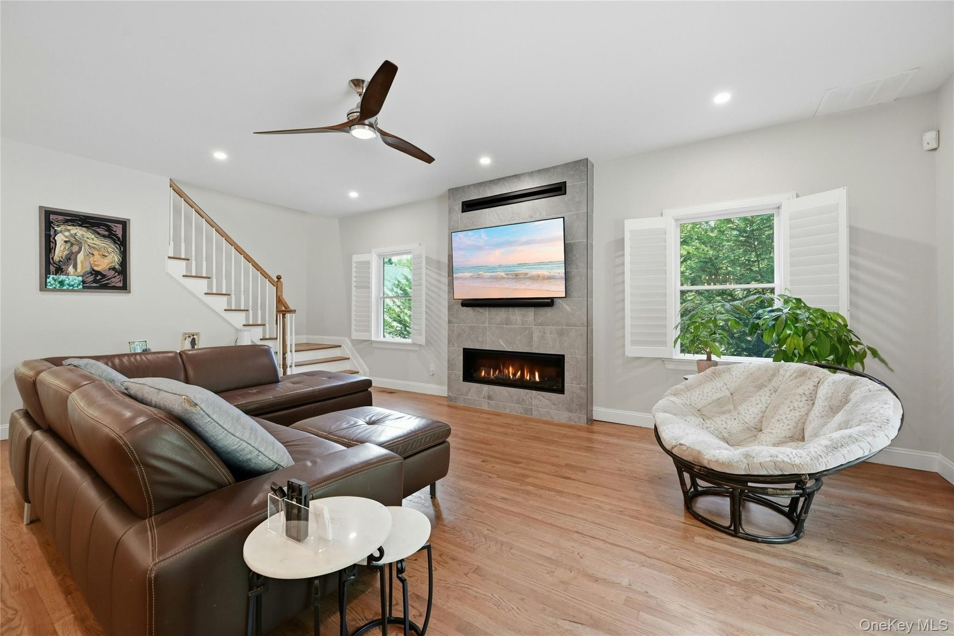 Open-concept living space featuring hardwood flooring, a contemporary ceiling fan, and a linear gas fireplace with stone surround and mounted televisi