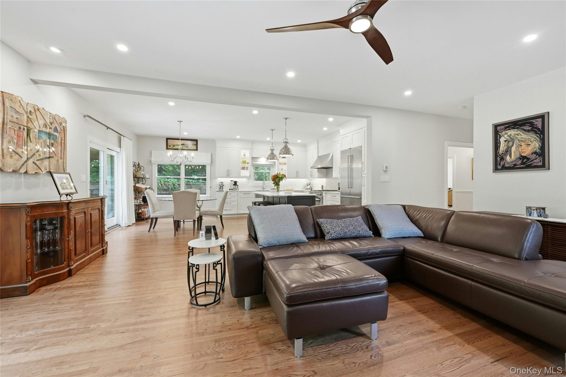 Open-concept living area featuring a brown leather sectional, wood-finish flooring throughout, and abundant recessed lighting