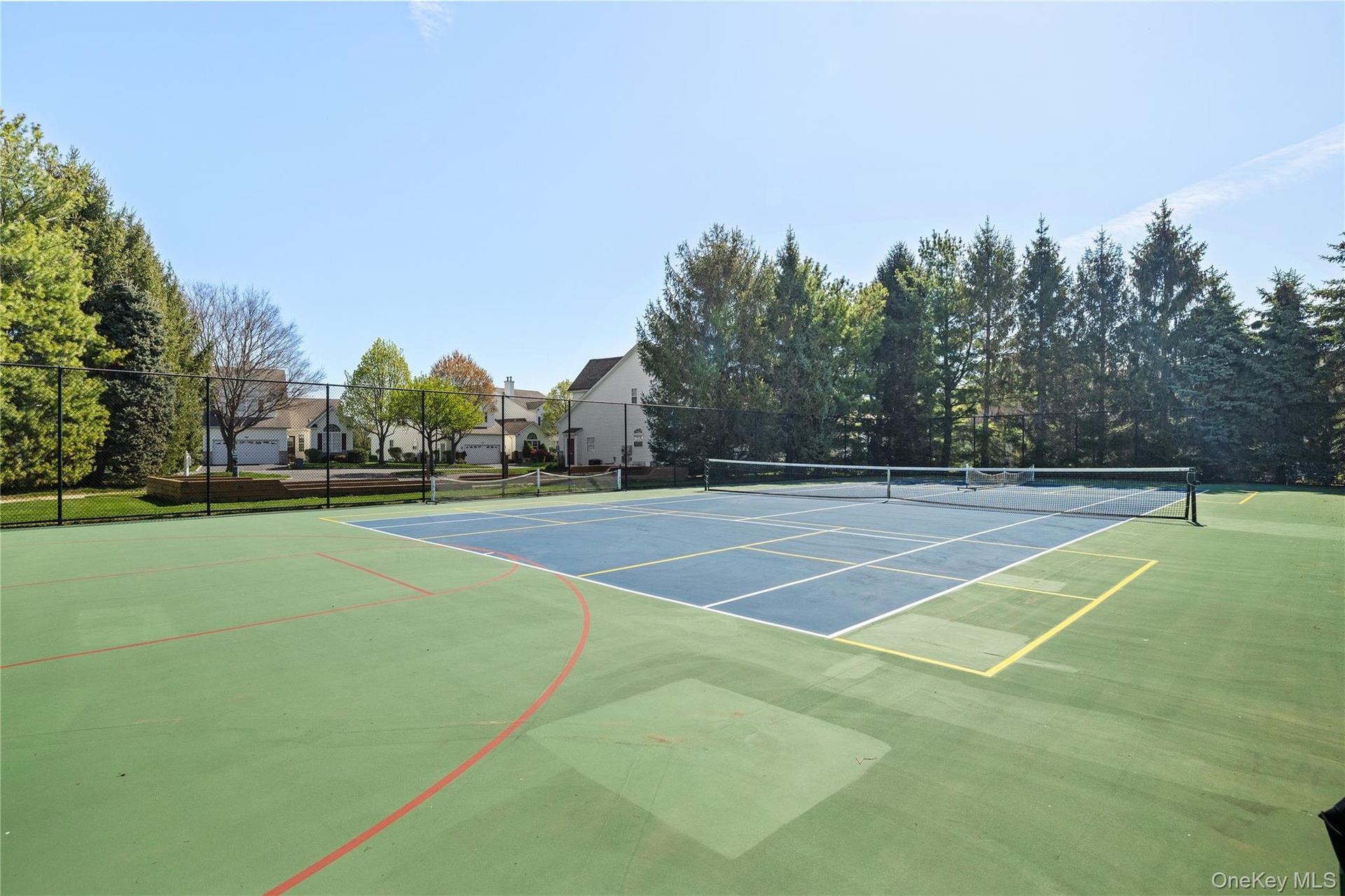 Full-sized tennis court with a perimeter fence, surrounded by mature trees