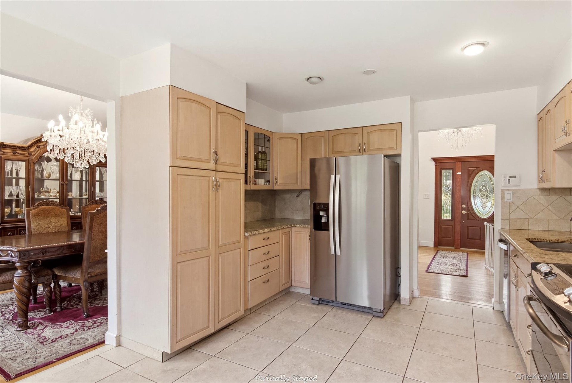 Kitchen featuring wood-finish cabinetry, tile flooring, stainless steel refrigerator, and granite countertops with tile backsplash