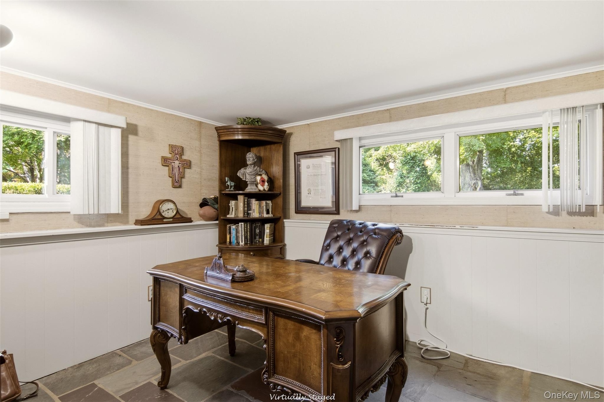 Sophisticated home office featuring a wood-finish desk with carved legs, built-in shelving with display space, large multi-pane windows with natural l