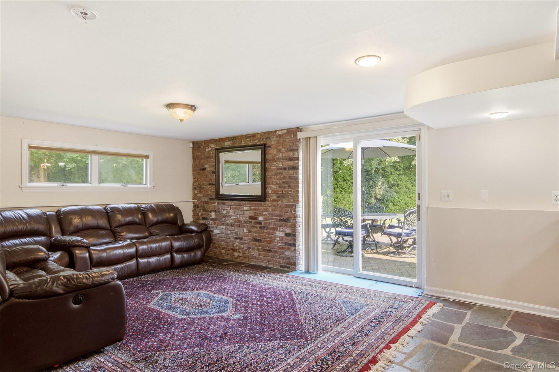 Exposed brick accent wall, recessed lighting, sliding glass door, multiple windows, and flagstone flooring