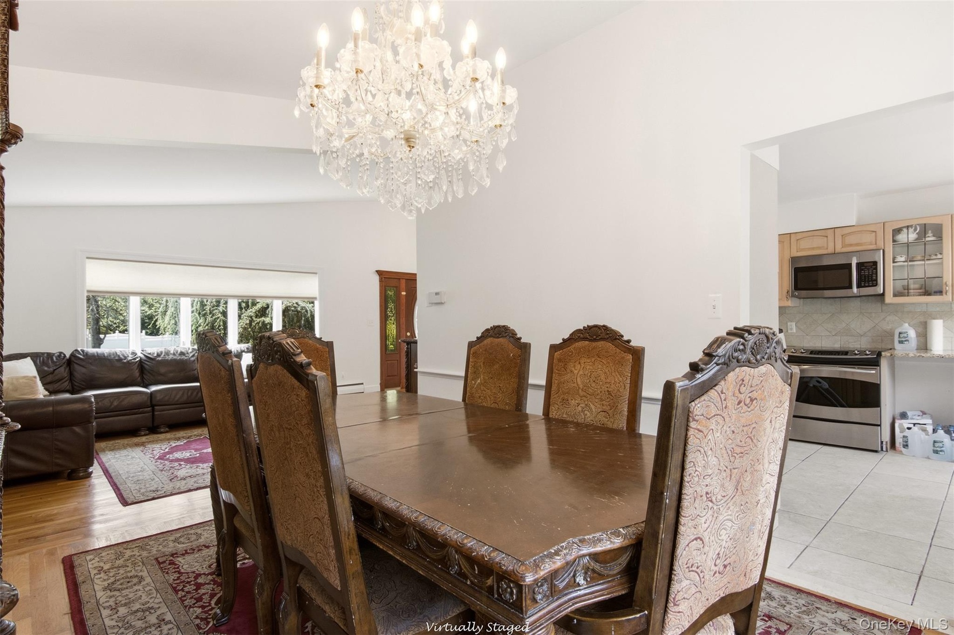 Vaulted ceiling with a crystal chandelier, wood-finish flooring, bay window, kitchen with stainless steel appliances, and wood cabinetry